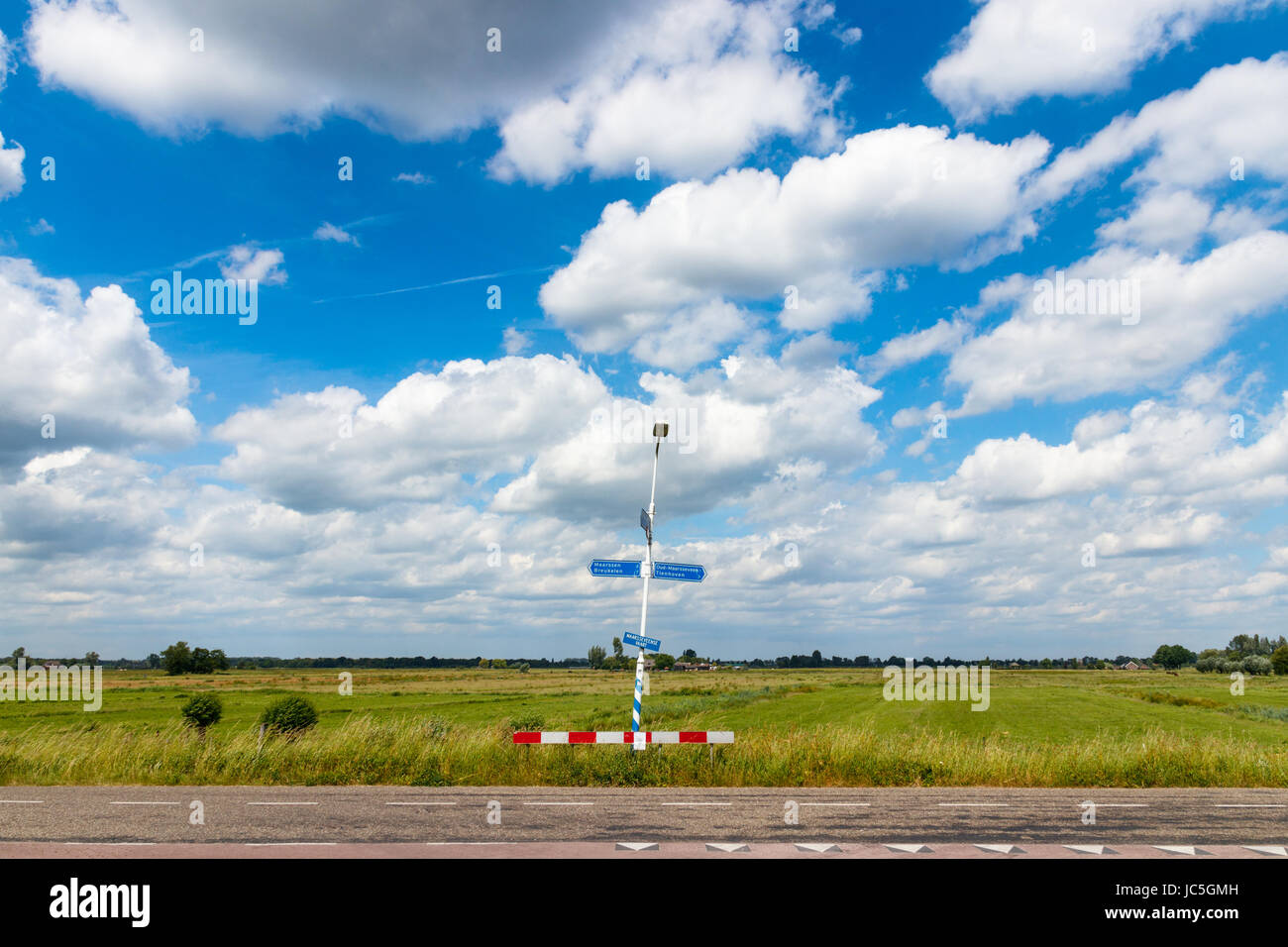 Tipico piatto olandese paesaggio con una vista su un polder e una strada con cartello stradale in una giornata di sole sotto un azzurro cielo nuvoloso. Maarsseveen, Paesi Bassi. Foto Stock