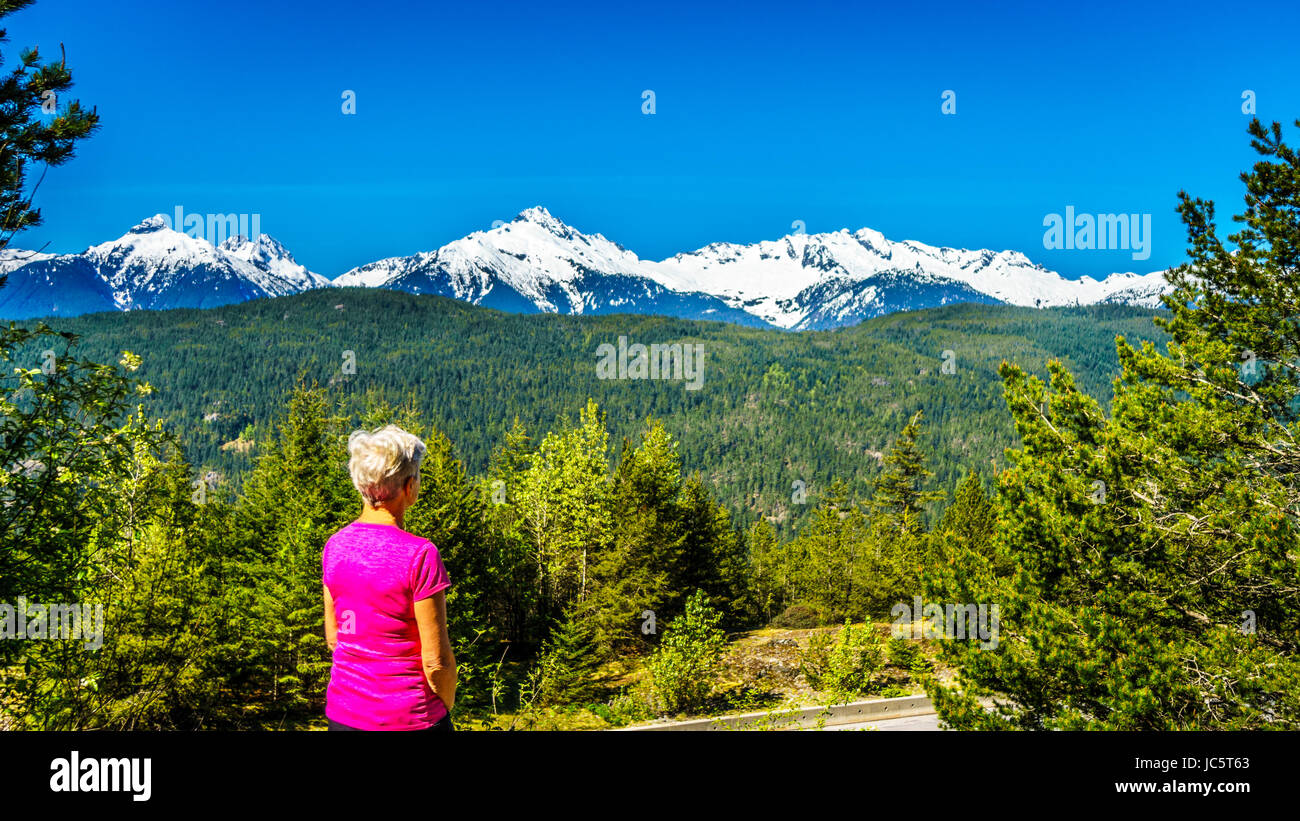 Una signora guardando le montagne innevate lungo l'autostrada 99, o il Sea to Sky Highway a Squamish, British Columbia, Canada Foto Stock