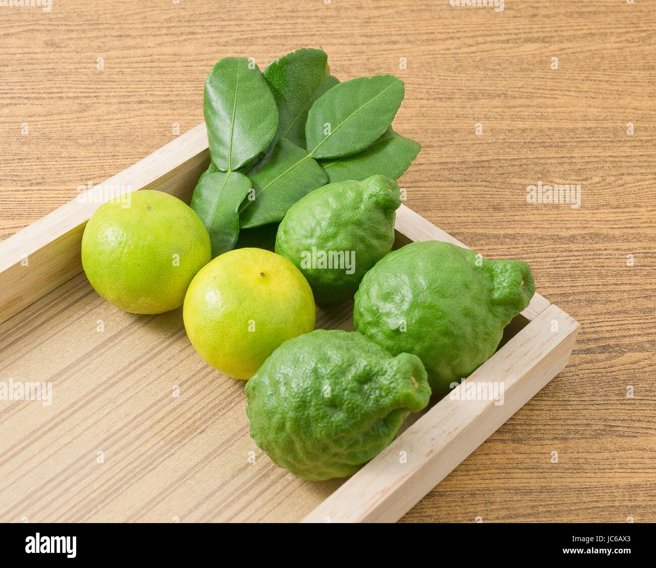 Vegetali e le erbe, Combava persiano con lime e foglie di Kaffir per condimento in cucina su un vassoio di legno. Foto Stock