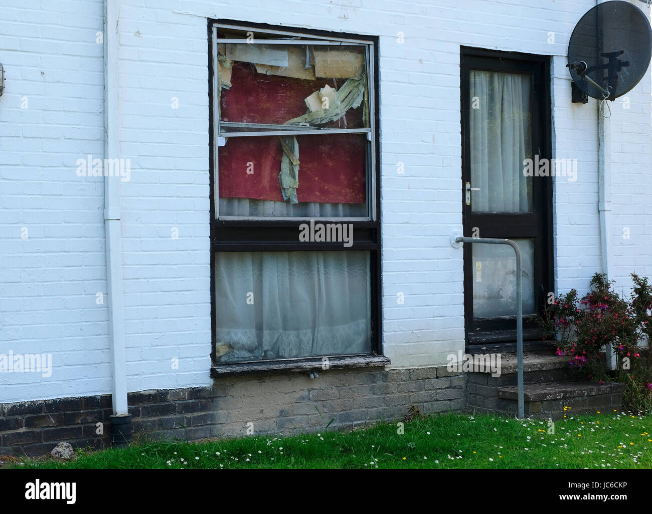 Mal mantenuta home crollato con telaio in alluminio windows farcite con carta e coperte per tenere fuori il freddo. West Sussex, Regno Unito Foto Stock