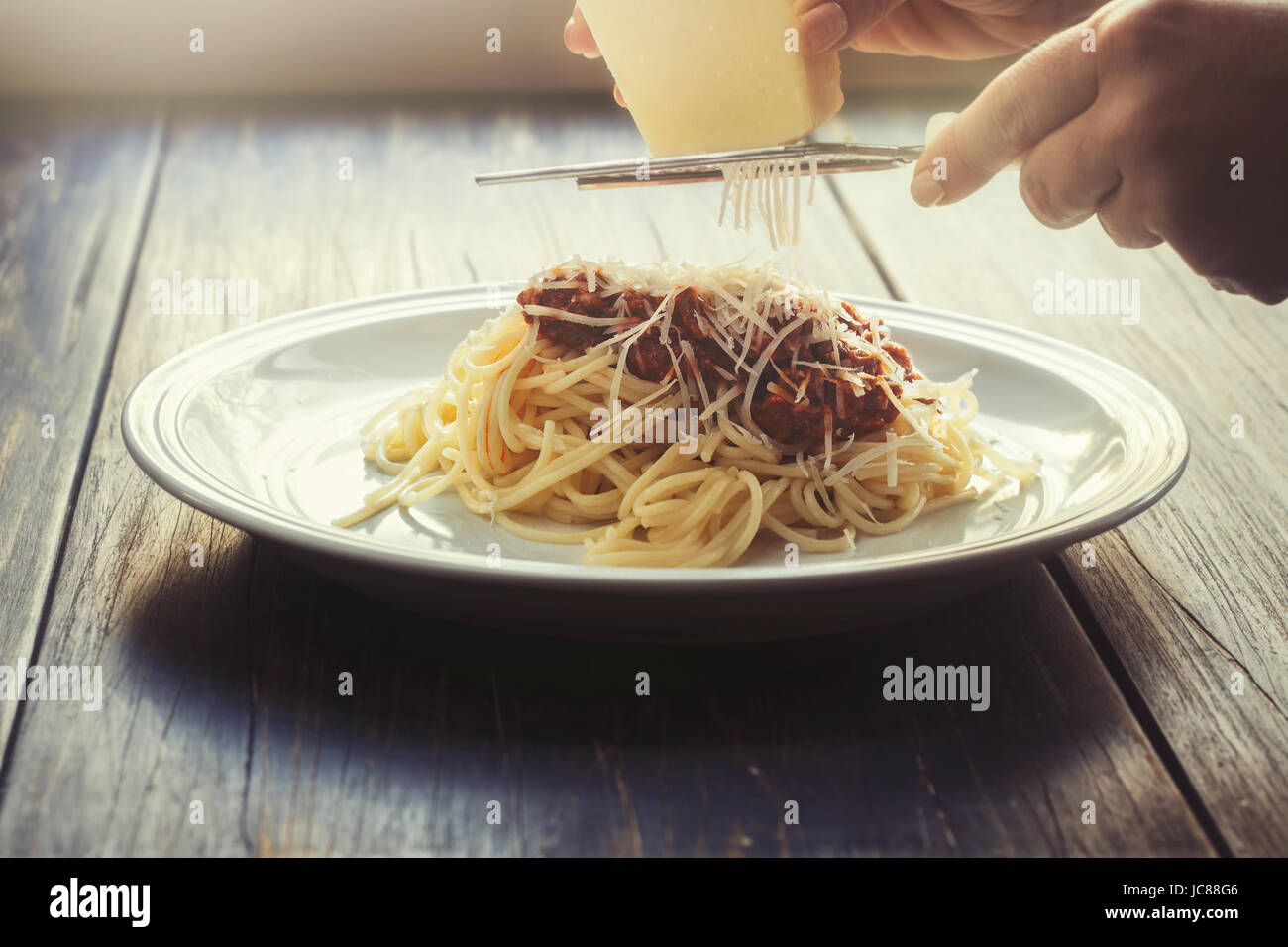 Cucinati freschi spaghetti alla bolognese su una piastra bianca e con mani femminili reticolo di formaggio parmigiano Foto Stock