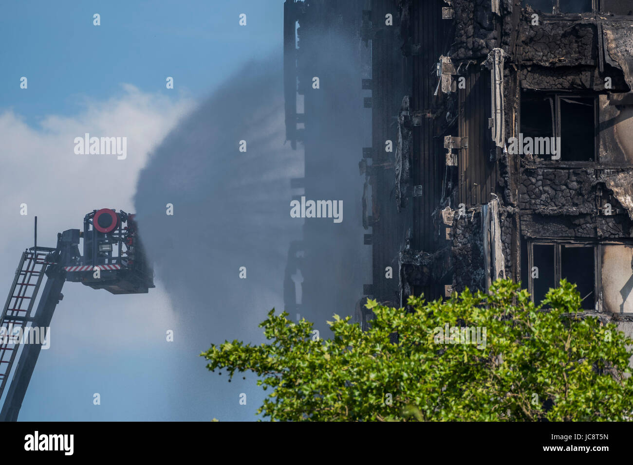 Londra, Regno Unito. 14 Giugno, 2017. Il servizio antincendio a getto di acqua tubi flessibili verso il basso la costruzione ma solo raggiunge circa a metà strada verso l'alto. Grenfell Tower - i resti carbonizzati della torre blocco che ha preso fuoco la scorsa notte in North Kensington vicino Latimer Road tube station. Londra 14 Giugno 2017. Credito: Guy Bell/Alamy Live News Foto Stock