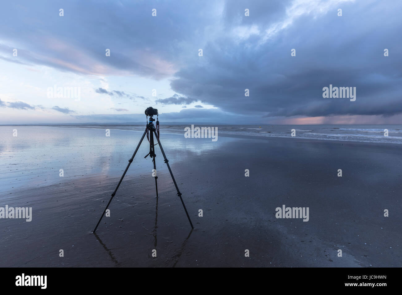 La fotocamera su un treppiede durante la bassa marea in spiaggia, in attesa di acquisire il tramonto Foto Stock