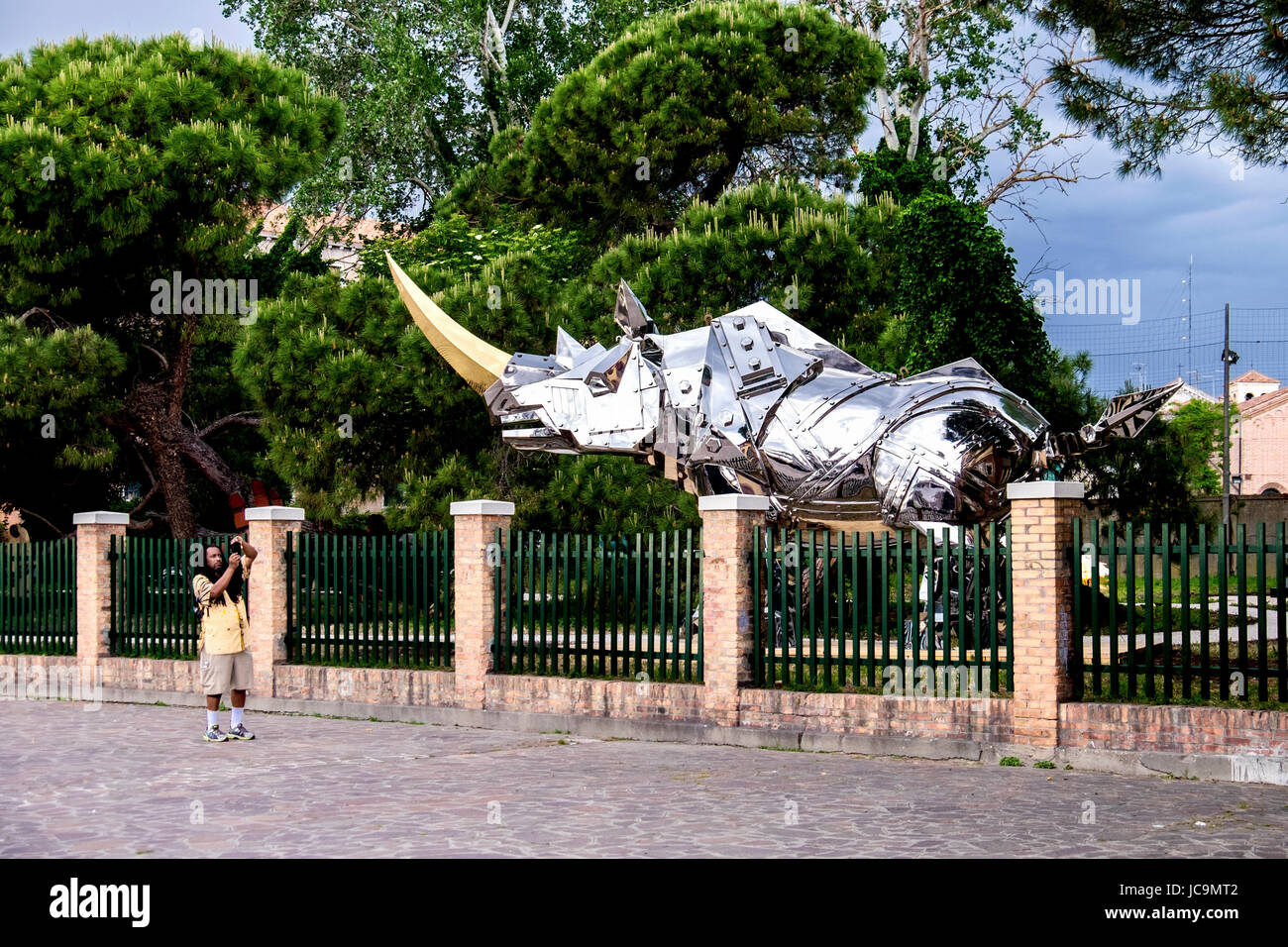 L'Italia,Venezia,Castello.Tourist prende foto di dimensioni di vita metallo lucido rhino in giardino durante il 2017 Biennale di Venezia. Rinoceronte metallico all'aperto Foto Stock