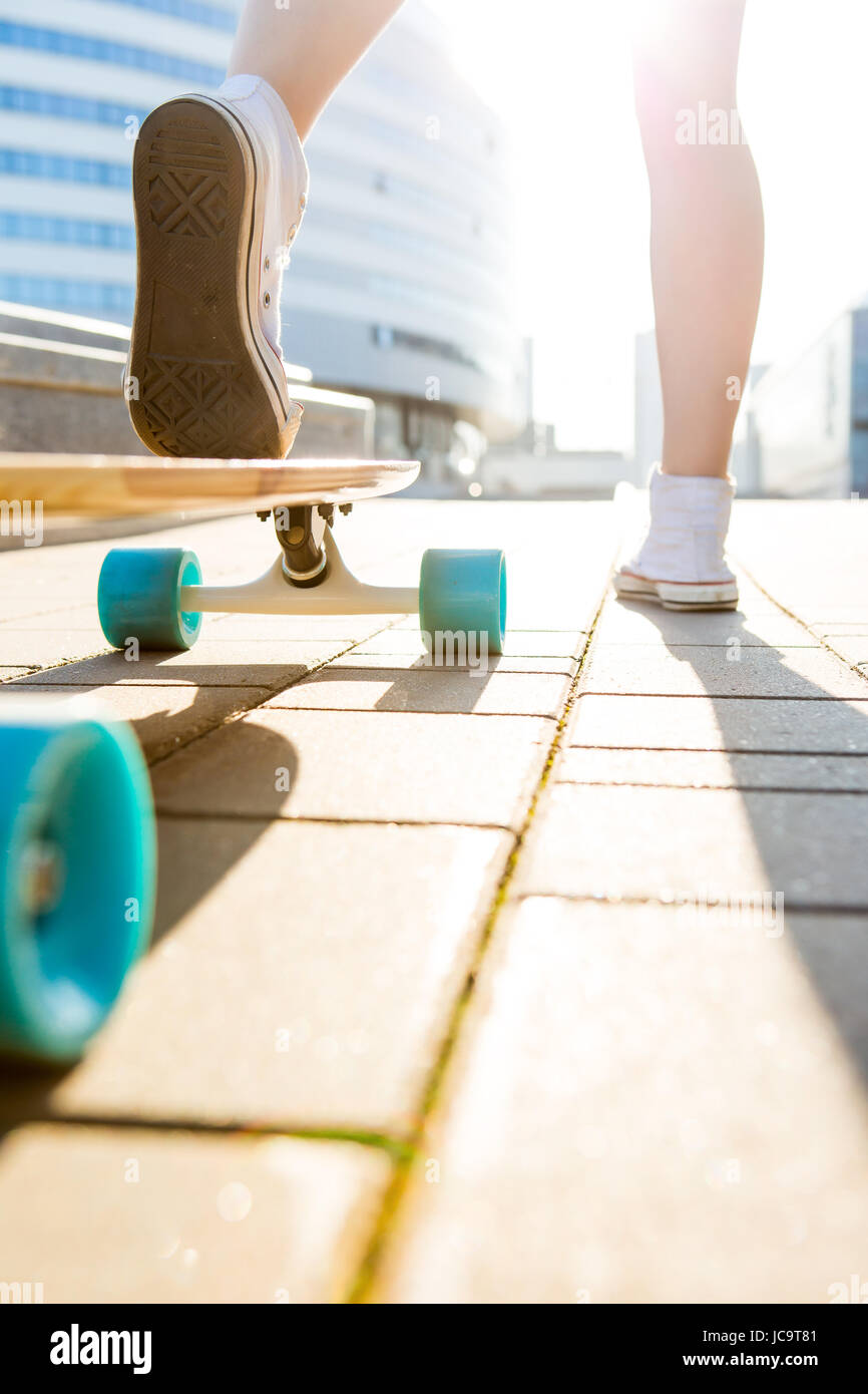 Close up sporty signora in bianco sneakers pronto a extreme funny cavalcare il suo pattino in legno longboard skateboard in luce del sole. Urbano moderno hipster ragazza ha Foto Stock