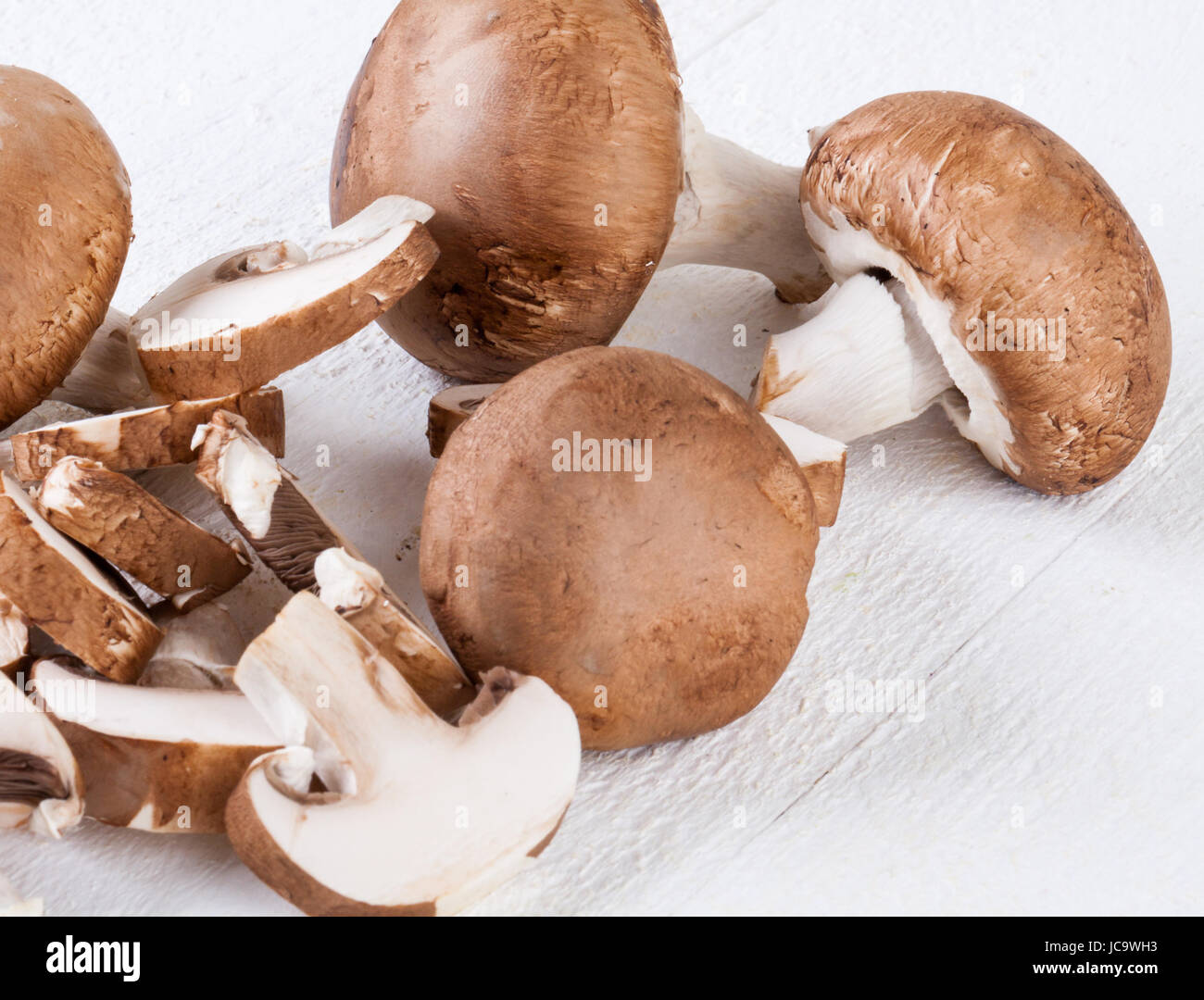 Frische Steinchampignons Champiggnons im ganzen und in Scheiben geschnitten auf einem weißen Holzbrett Foto Stock