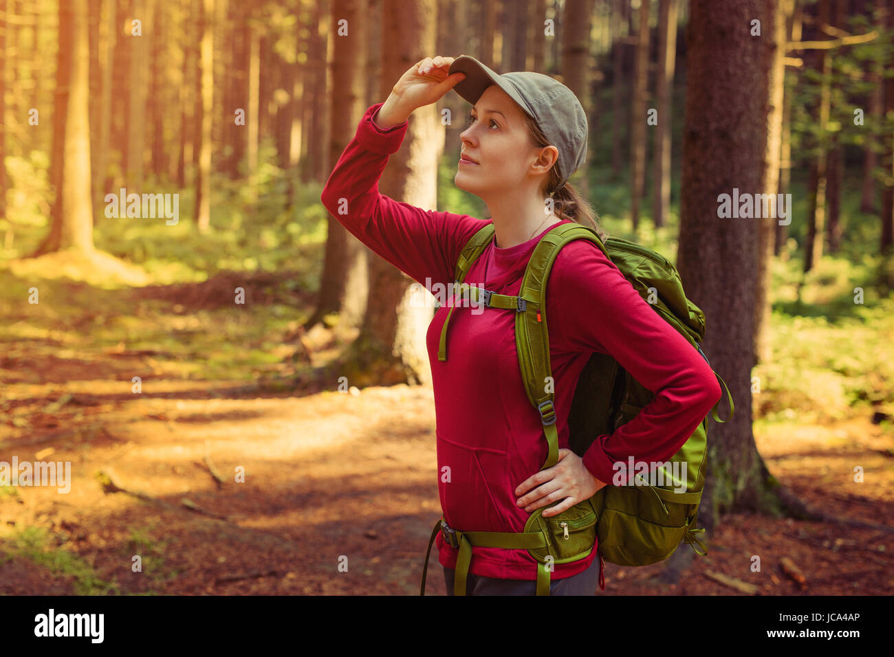 Giovane donna turista in rosso abbigliamento con zaino verde cercando riposo nella foresta Foto Stock