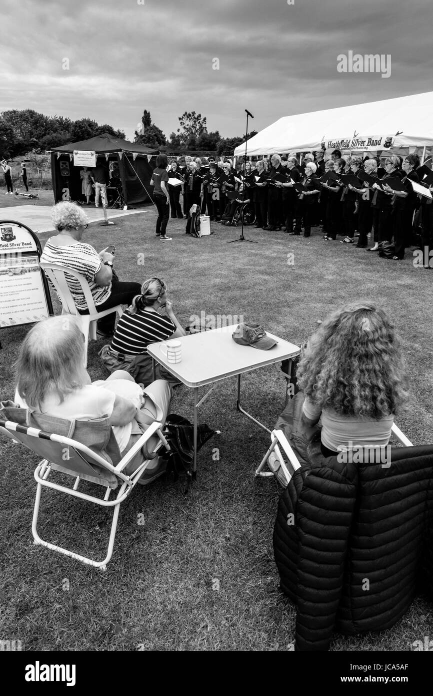 La popolazione locale guarda una comunità coro cantando sotto la pioggia a Maresfield Fete, Maresfield, East Sussex, Regno Unito Foto Stock