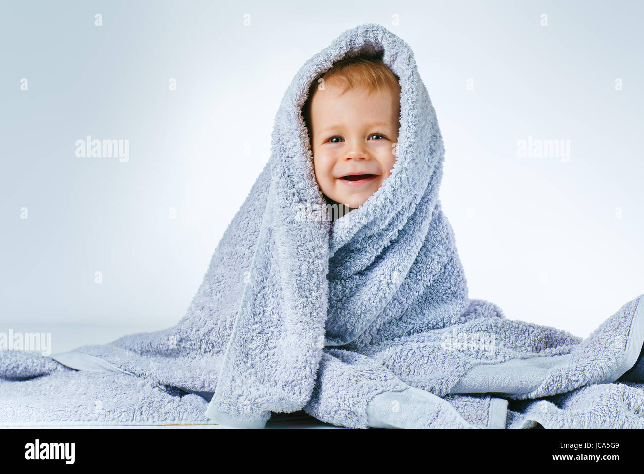 Gli otto mesi baby dopo lavaggio in seduta grande asciugamano morbido e sorridente su sfondo bianco Foto Stock
