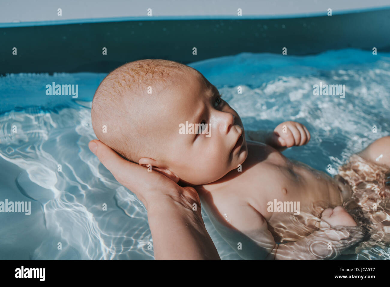 Baby cercando di nuotare in piscina con la madre aiutare Foto Stock