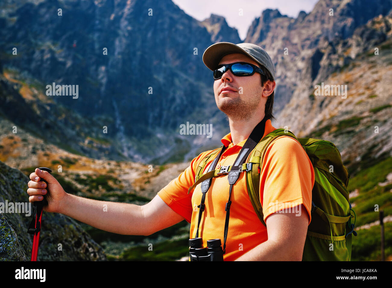 Uomo giovani turisti con zaino verde e occhiali da sole ritratto su alte montagne sullo sfondo Foto Stock