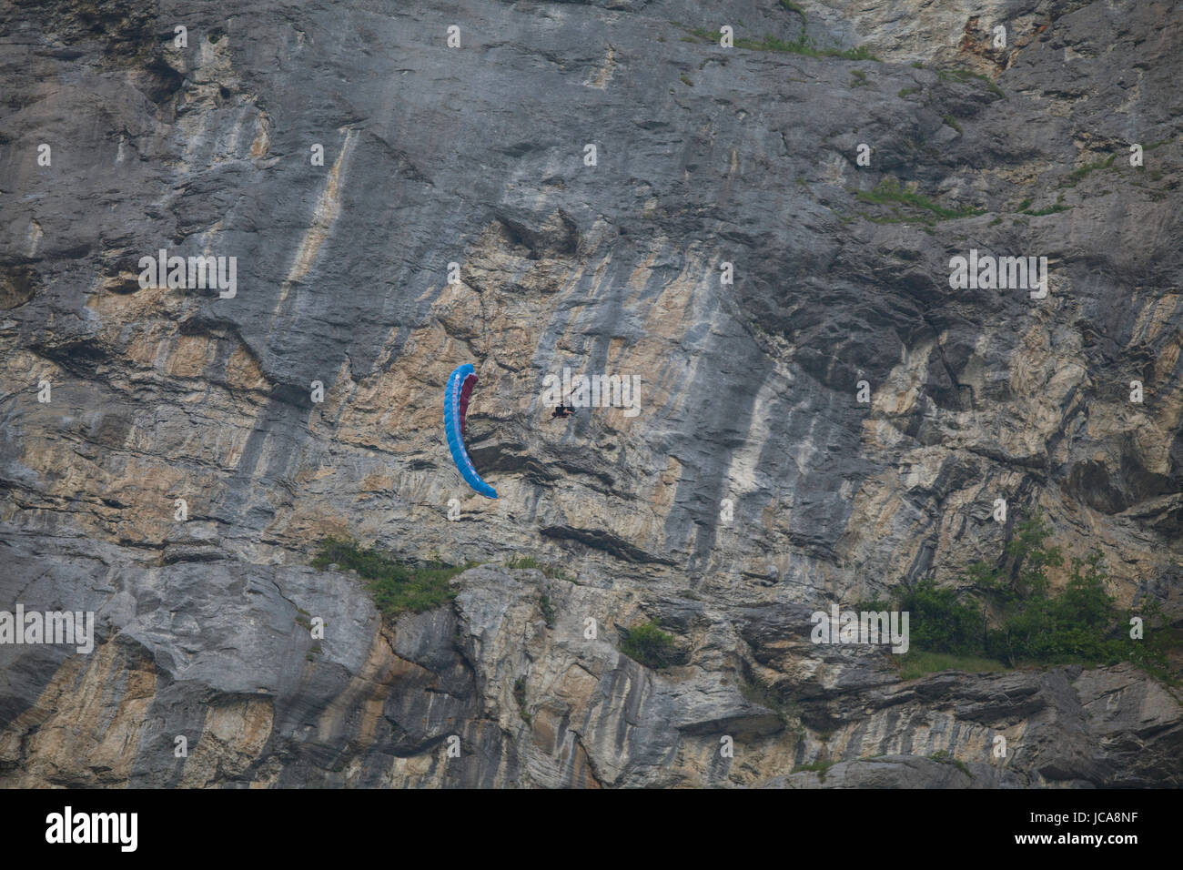 Una persona non identificata fare acrobazie con un parawing davanti a un enorme roccia. Lauterbrunnen, Svizzera. Foto Stock
