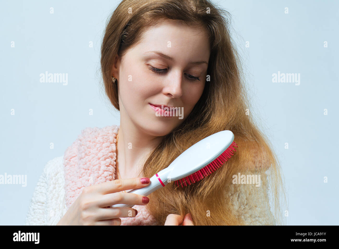 Giovane donna bionda in accappatoio pettinare i capelli dopo il lavaggio. Su sfondo bianco. Foto Stock