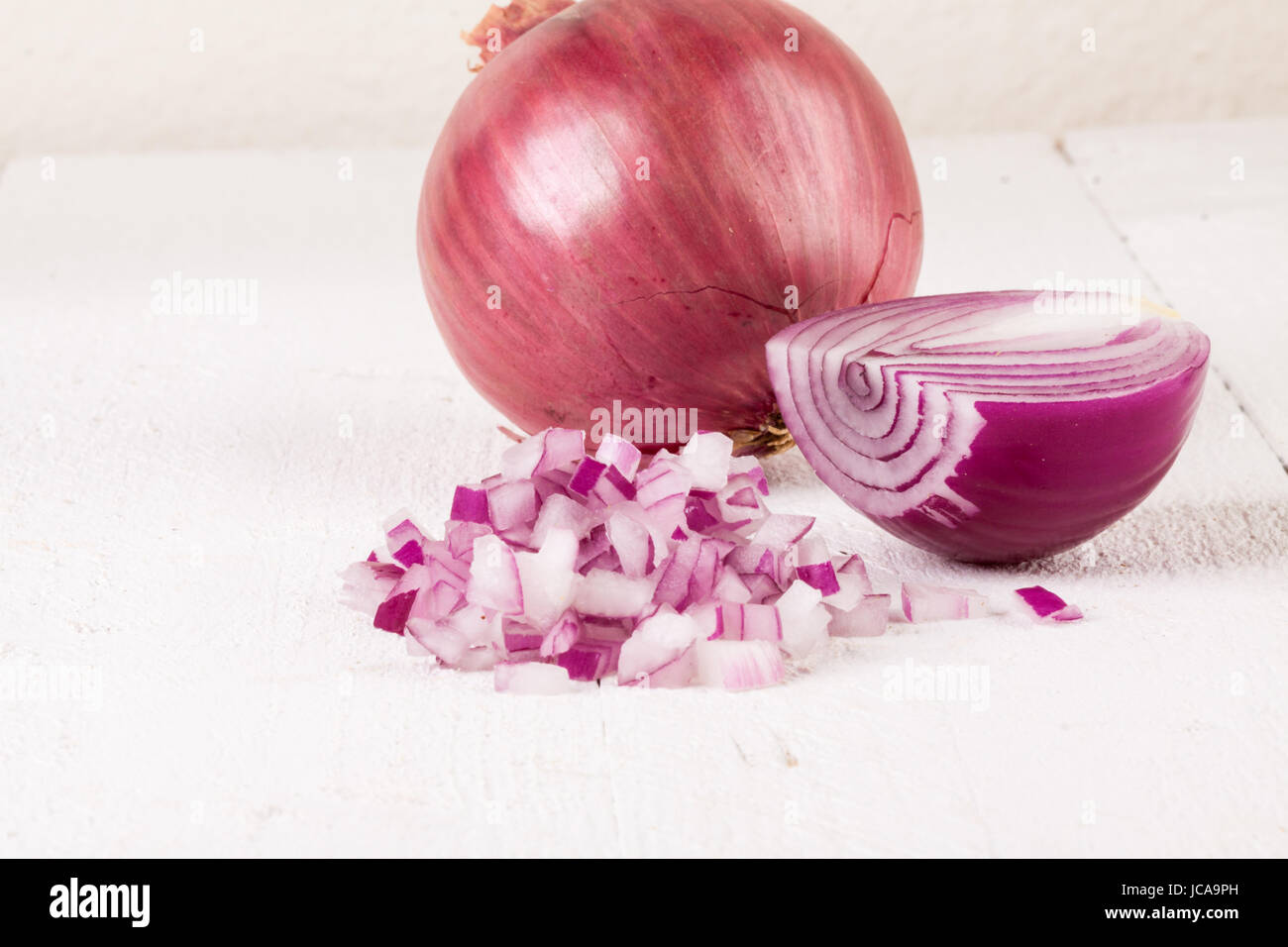 Rote Speise Zwiebel im ganzen und in kleinen Würfeln Brunoise in einer Schale auf einem weißen Holzbrett Foto Stock