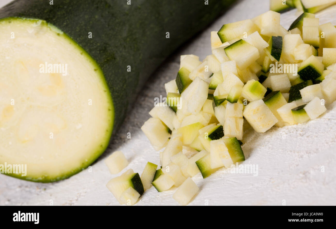 Frische Zucchine im ganzen in julienne streifen und in brunoise würfeln geschnitten auf einem weißen Hoözbrett Foto Stock