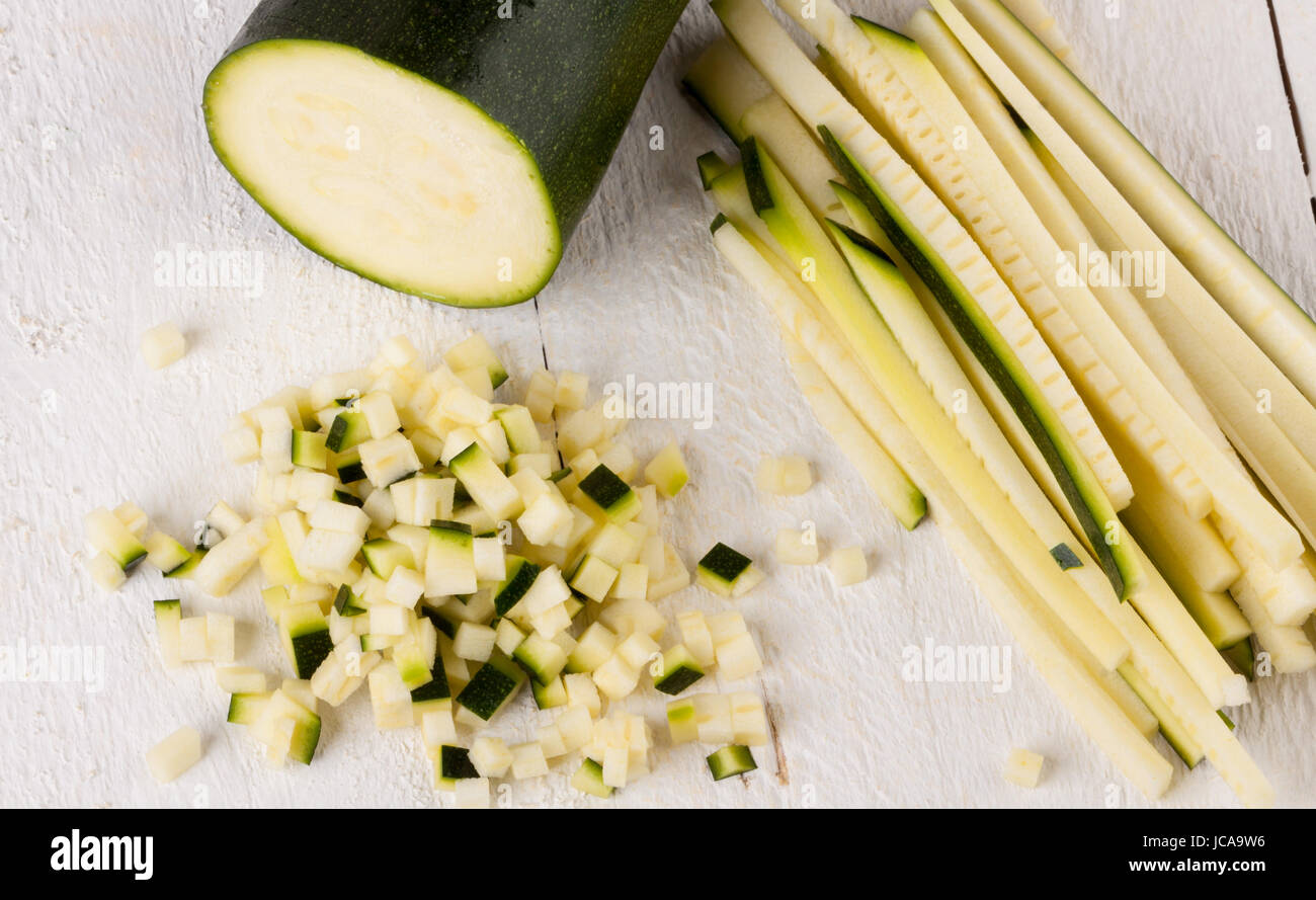 Frische Zucchine im ganzen in julienne streifen und in brunoise würfeln geschnitten auf einem weißen Hoözbrett Foto Stock