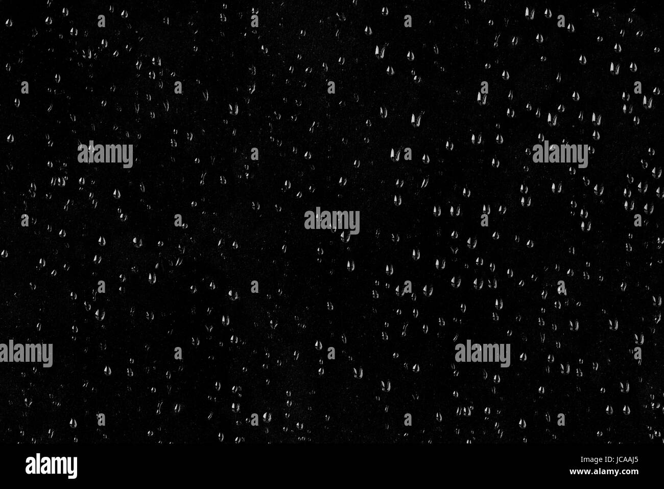 Gocce d'acqua sul vetro sporco su sfondo scuro. Foto Stock