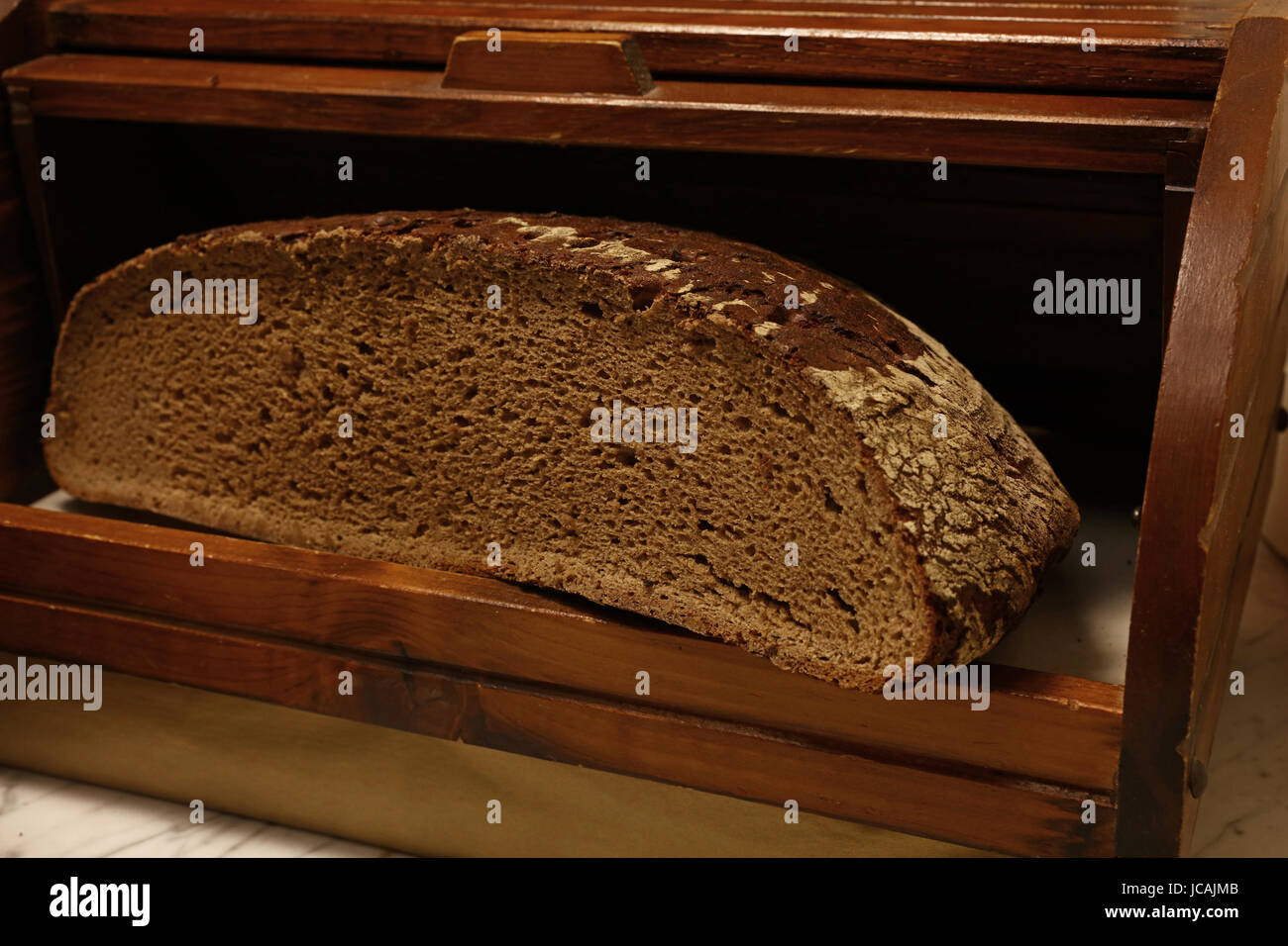 La metà degli artigiani nero scuro fresca Pane di segale pane in stile rustico tradizionale in legno vintage breadbin box, chiudere fino a basso angolo di visione Foto Stock