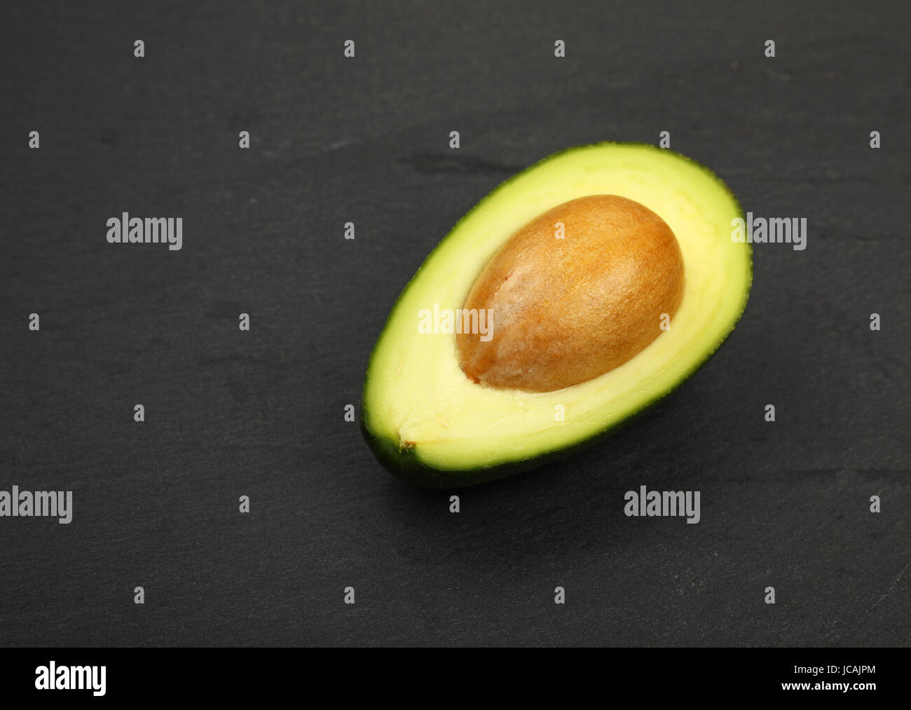 Una matura fresca verde metà di avocado con pit su pietra ardesia nera sullo sfondo della scheda, dettaglio, vicino ad alto angolo di visione Foto Stock