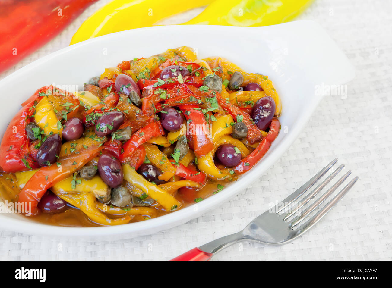 Peperoni cotto in padella con olio, olive e capperi. Cucina tipica italiana, pronto a mangiare. Ciotola bianco su sfondo bianco. Foto Stock