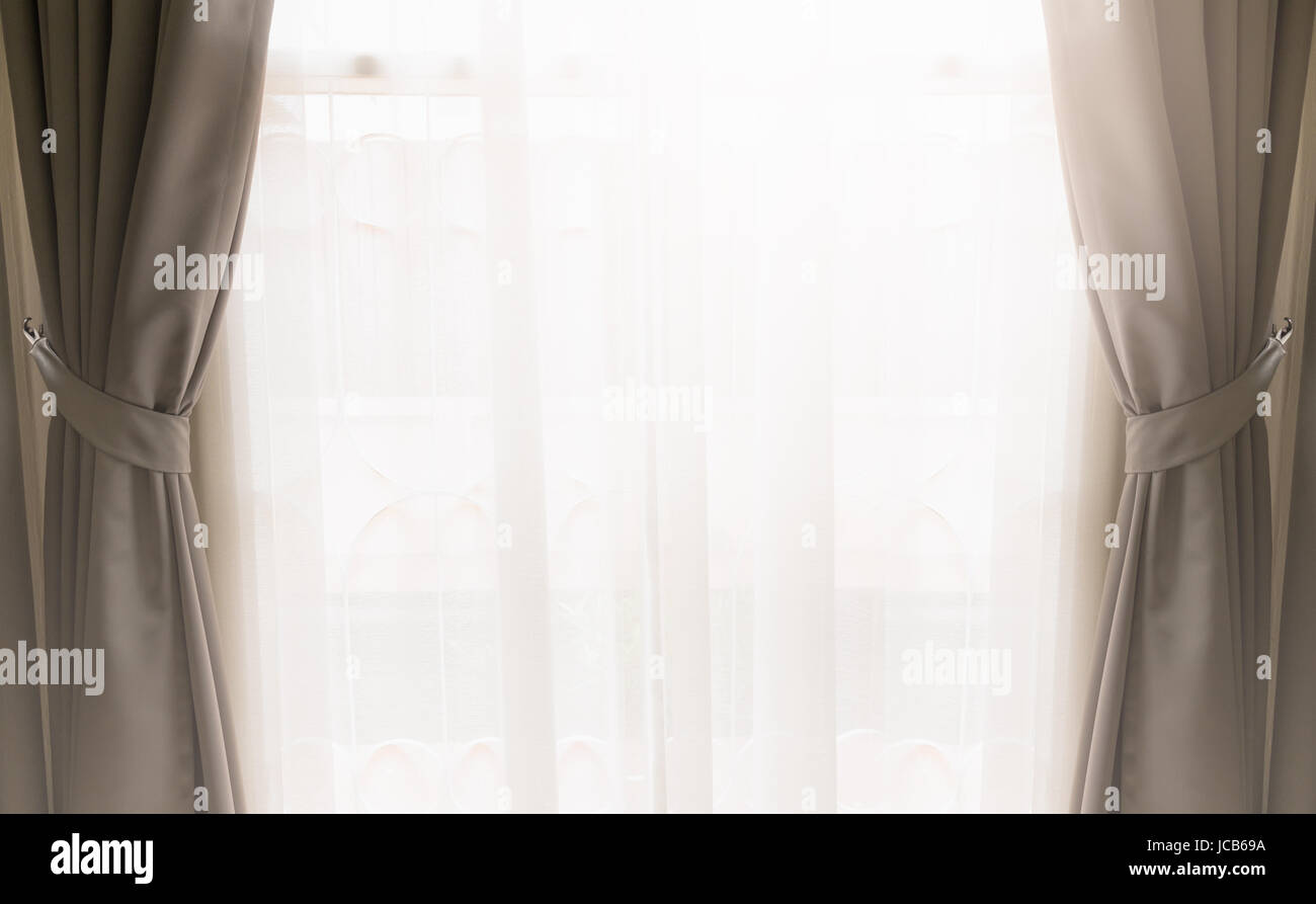 Aprire la tendina di seta in color crema sulla copertura per una finestra da vedere attraverso la tenda bianca con brillante luce dall'esterno. Foto Stock