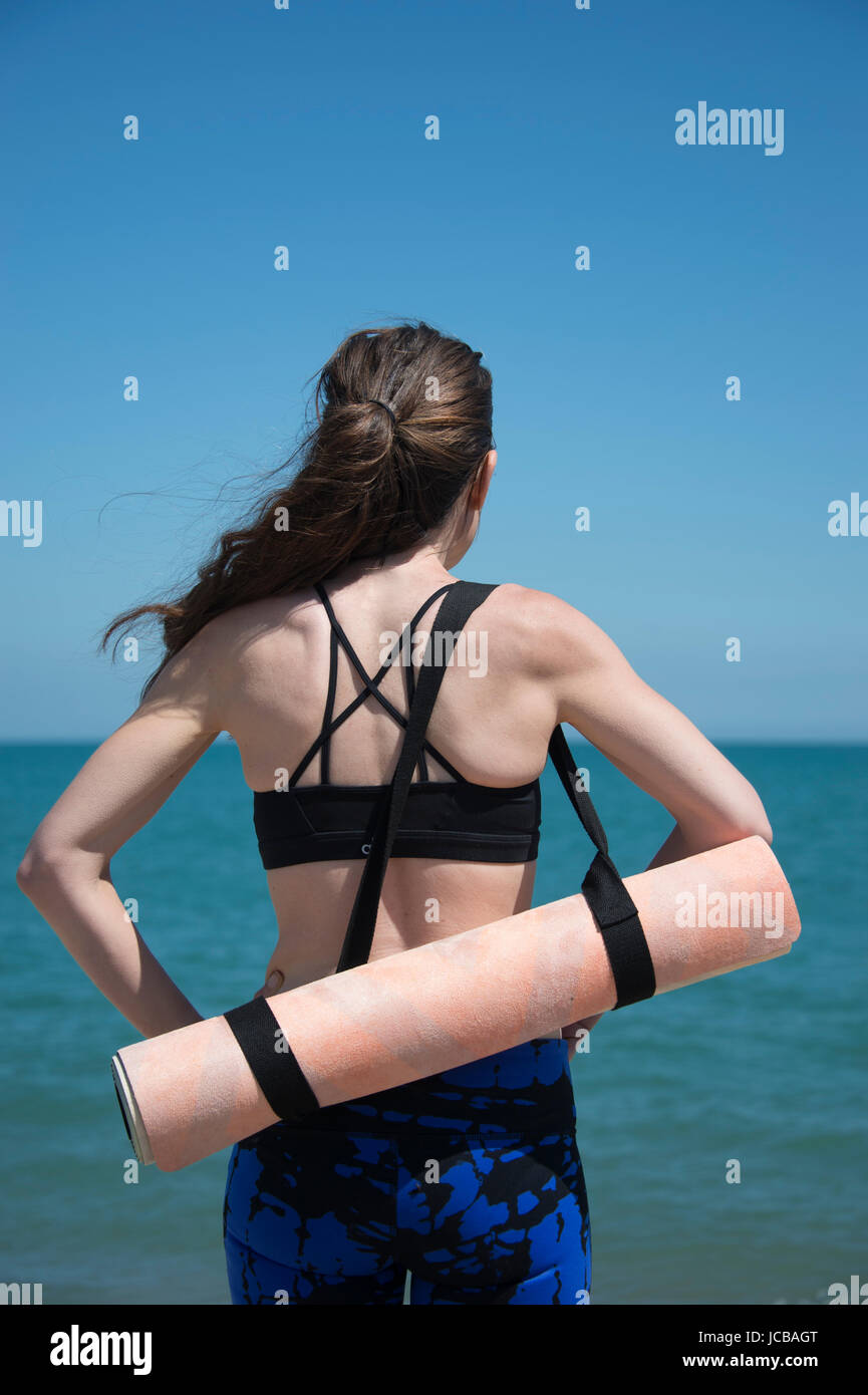 La donna che porta un materassino yoga in spiaggia Foto Stock