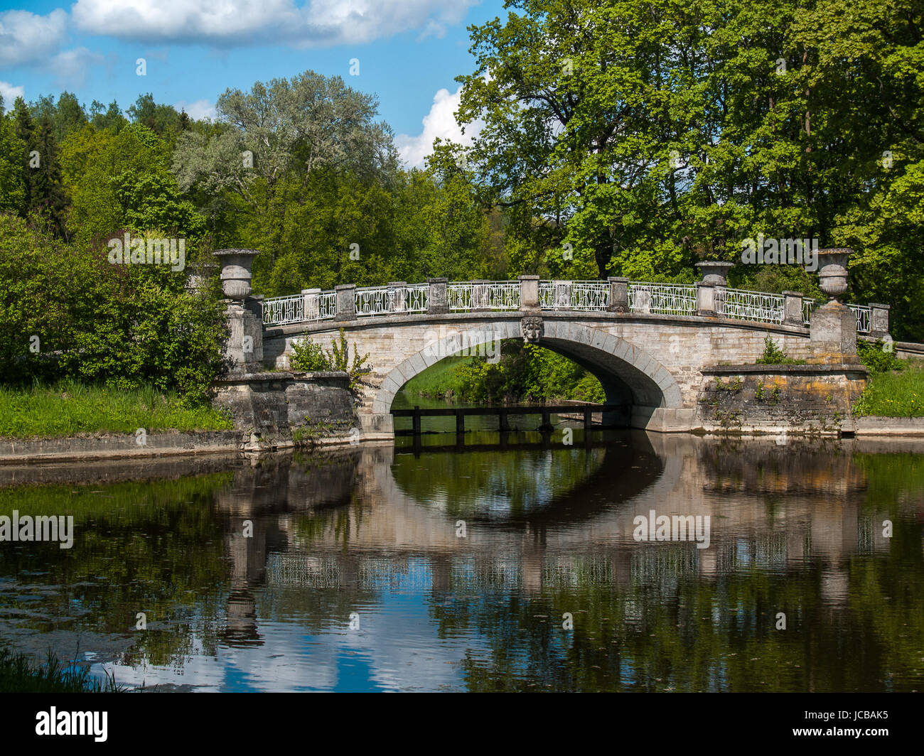 Paesaggio con un ponte in pietra nel verde degli alberi in un pomeriggio di estate nel parco della città Foto Stock