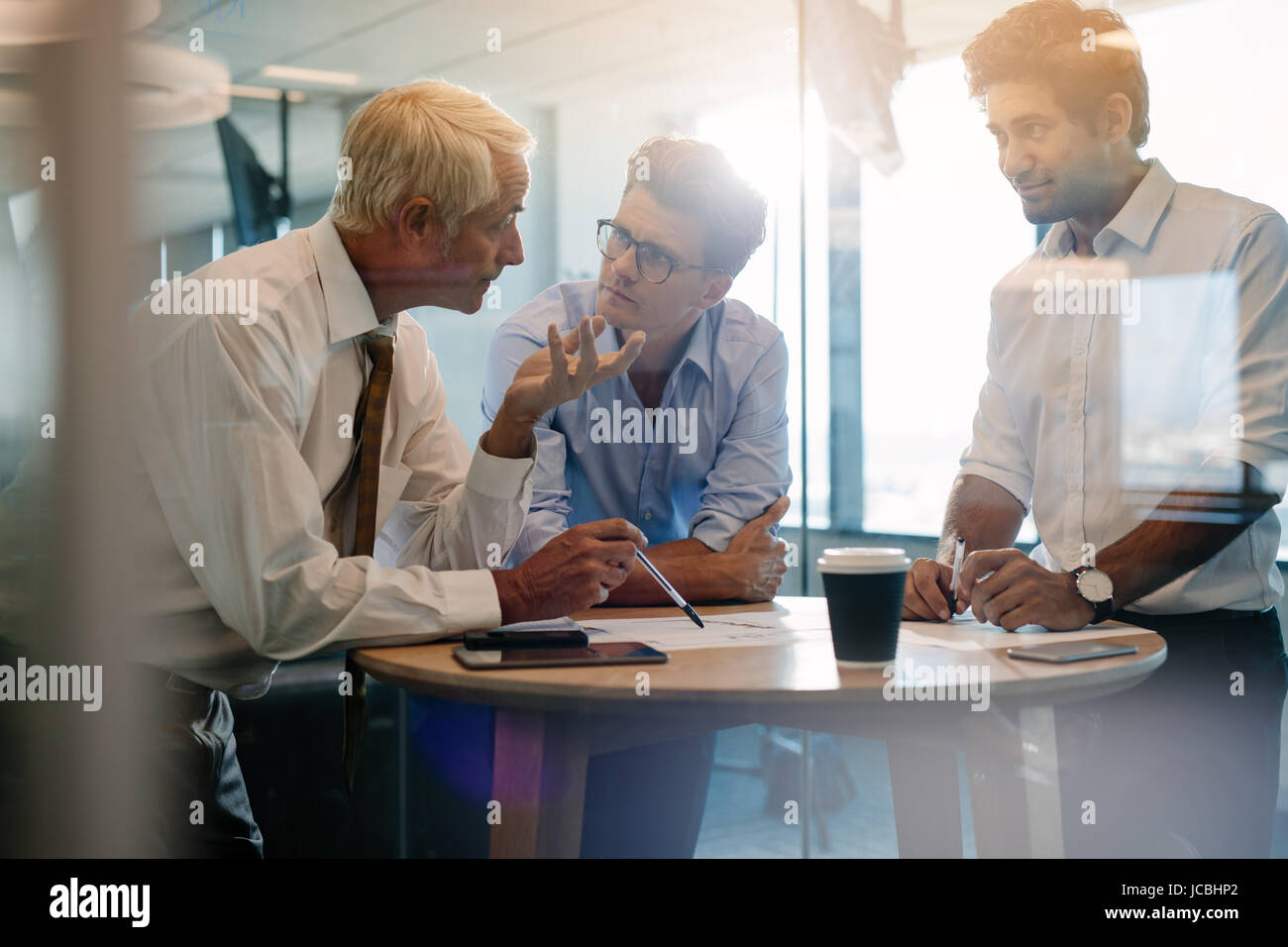 Tre dirigenti maschi in piedi e discutere attorno ad un tavolo. Professionista aziendale avente un incontro informale in un ufficio moderno. Foto Stock