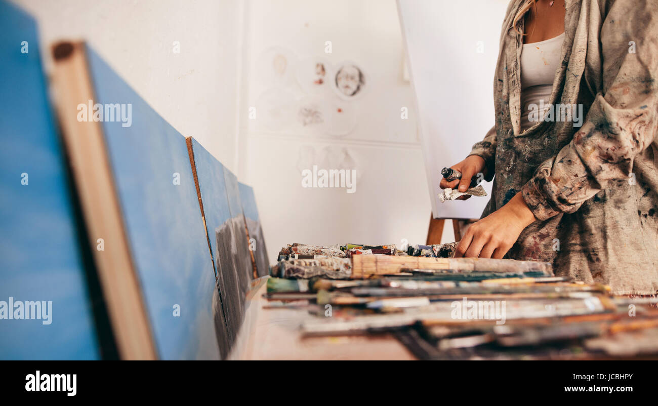 Ritagliato colpo di artista femminile di prelevare gli strumenti e i tubi di colore dalla tabella. Donna che lavorano nel suo studio. Foto Stock