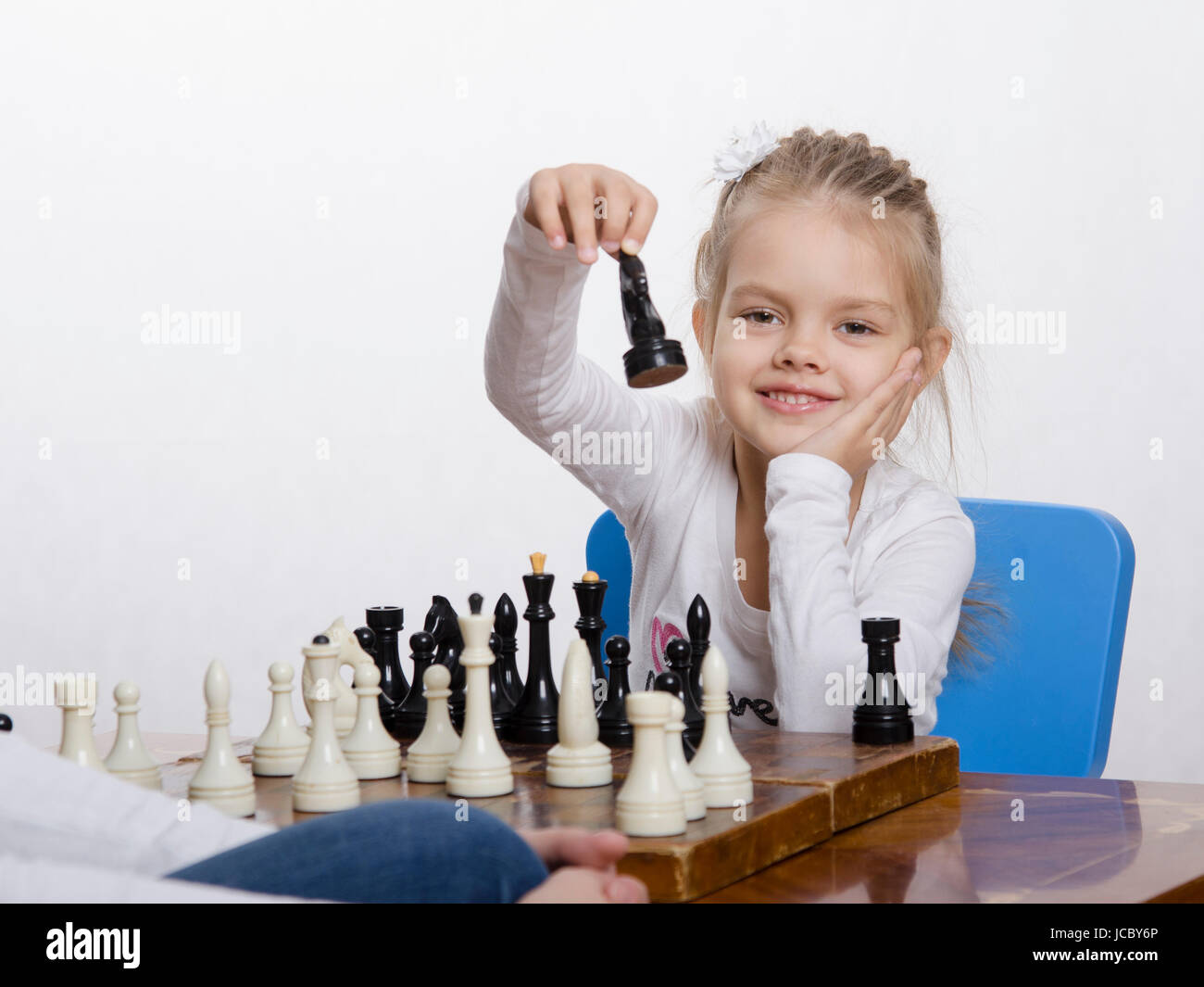 Quattro-anno-vecchia ragazza che gioca a scacchi. Ragazza in cerca di divertimento nel telaio con la figura in mano, si prepara a fare una mossa Foto Stock