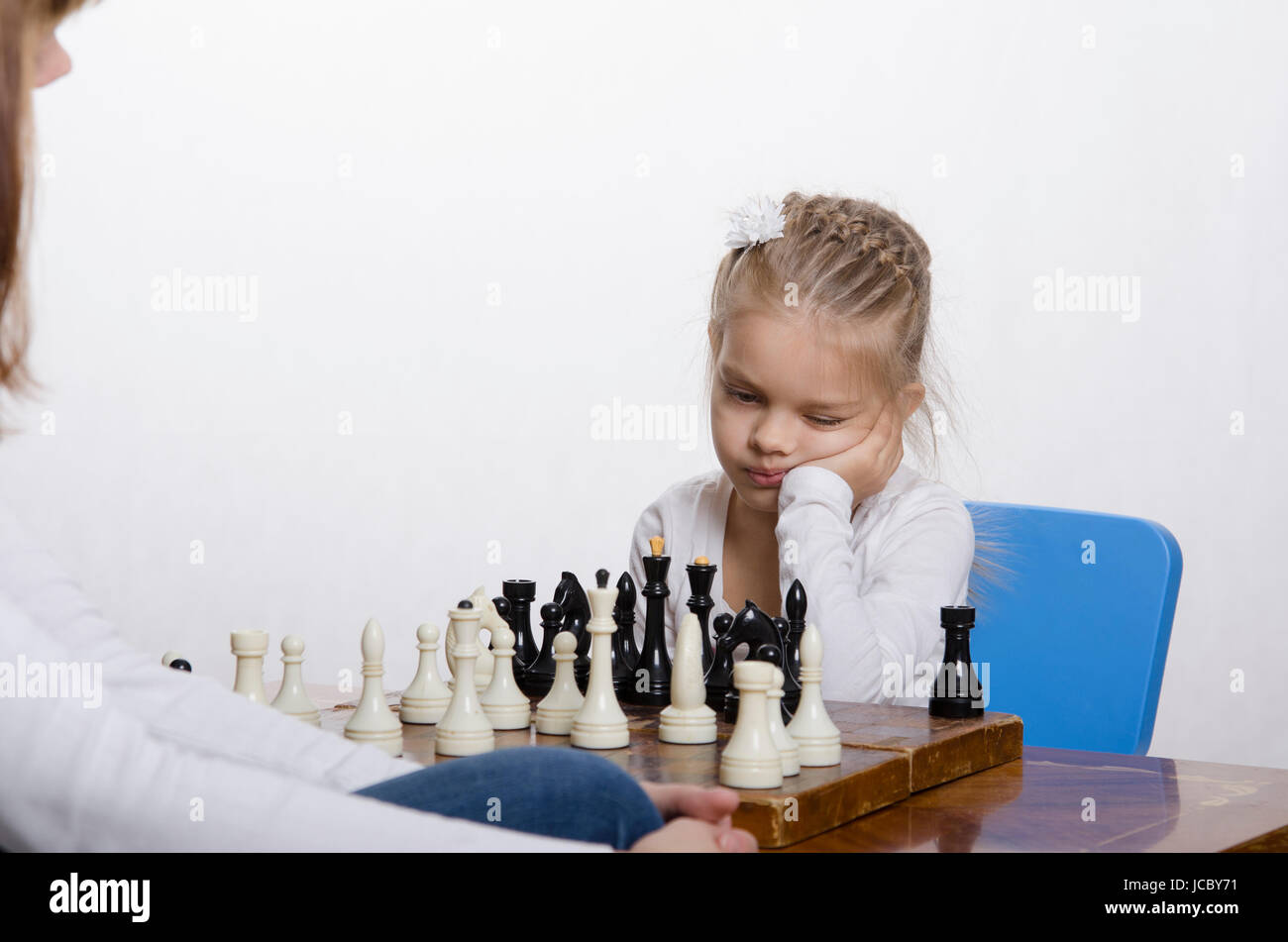 Quattro-anno-vecchia ragazza che gioca a scacchi. Ragazza in cerca di divertimento nel telaio con la figura in mano, si prepara a fare una mossa Foto Stock