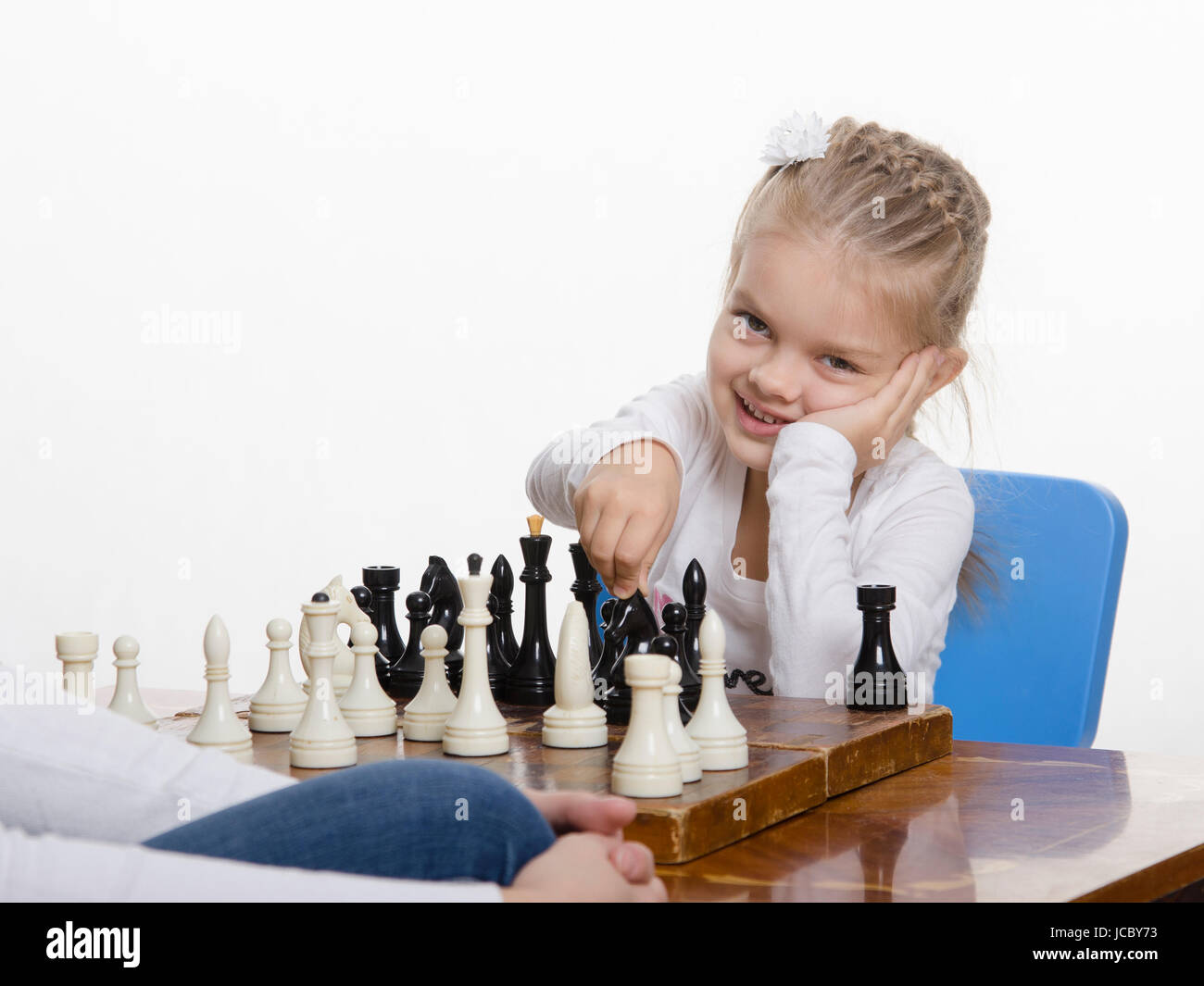 Quattro-anno-vecchia ragazza che gioca a scacchi. Ragazza in cerca di divertimento nel telaio con la figura in mano, si prepara a fare una mossa Foto Stock