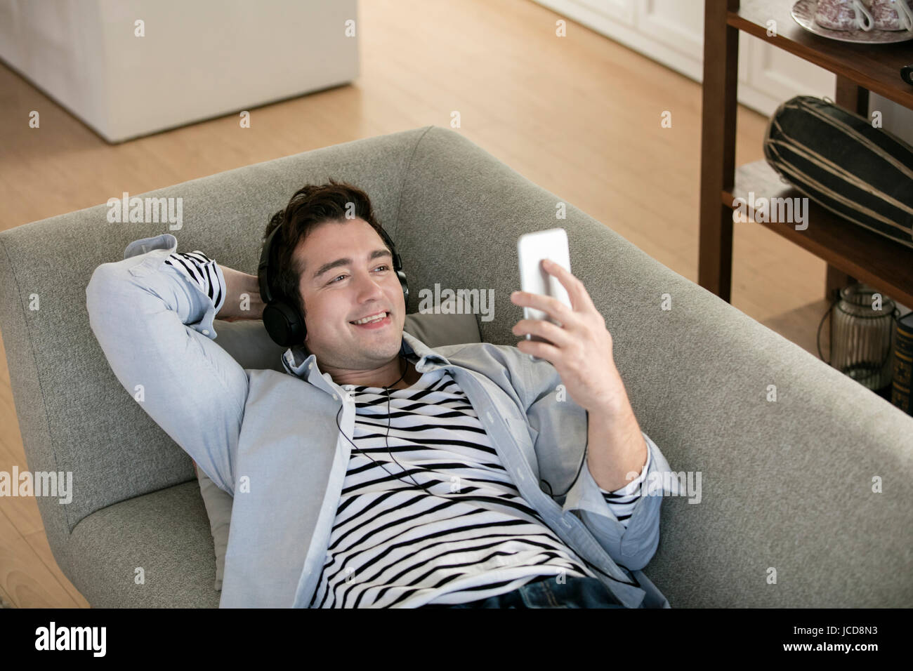 Sorridente uomo occidentale utilizza lo smartphone rilassante sul divano Foto Stock