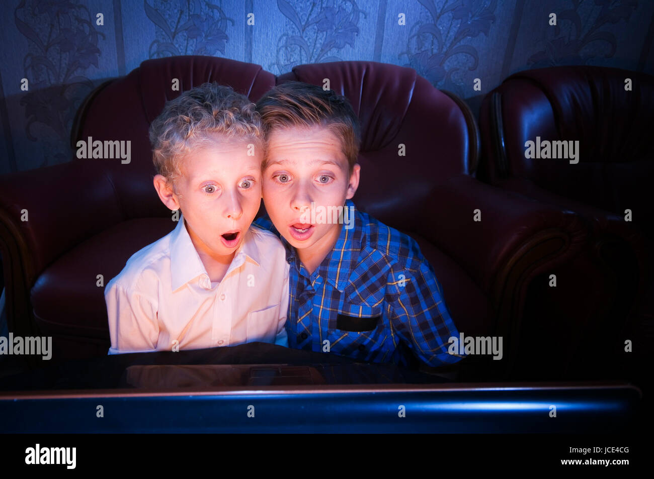 Frontale Ansicht zweier Brüder im Alter von 7 und 13 Jahren abgedunkelten im Zimmer schockiert in den Fernseher blickend Foto Stock