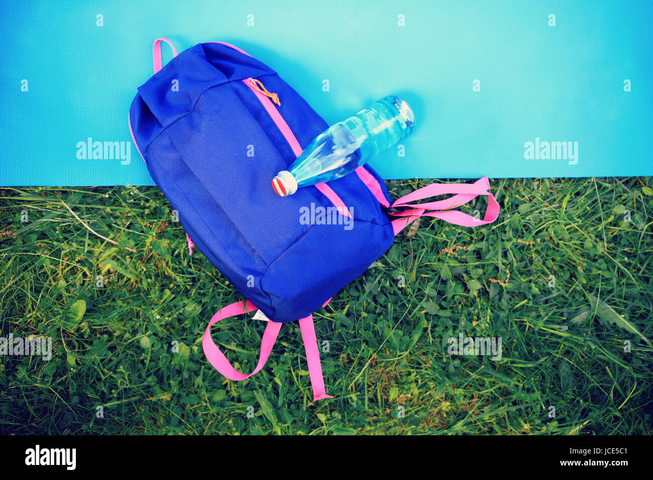 Estate sfondo sportivo. Bottiglia di acqua e uno zaino sul tappetino palestra di sopra sull'erba verde dello sfondo. Foto Stock