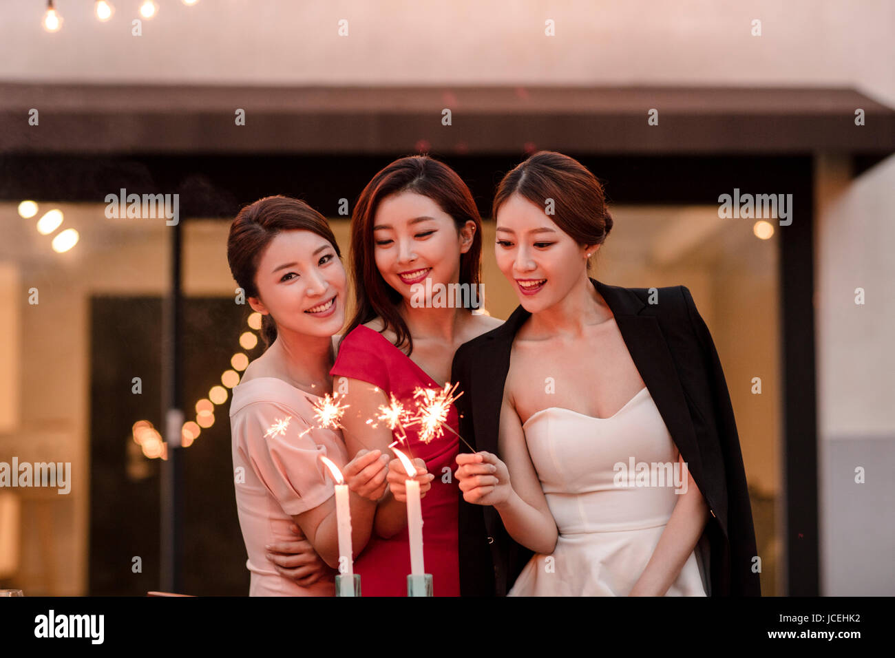 Tre giovani donne sorridenti accendendo candele a parte Foto Stock