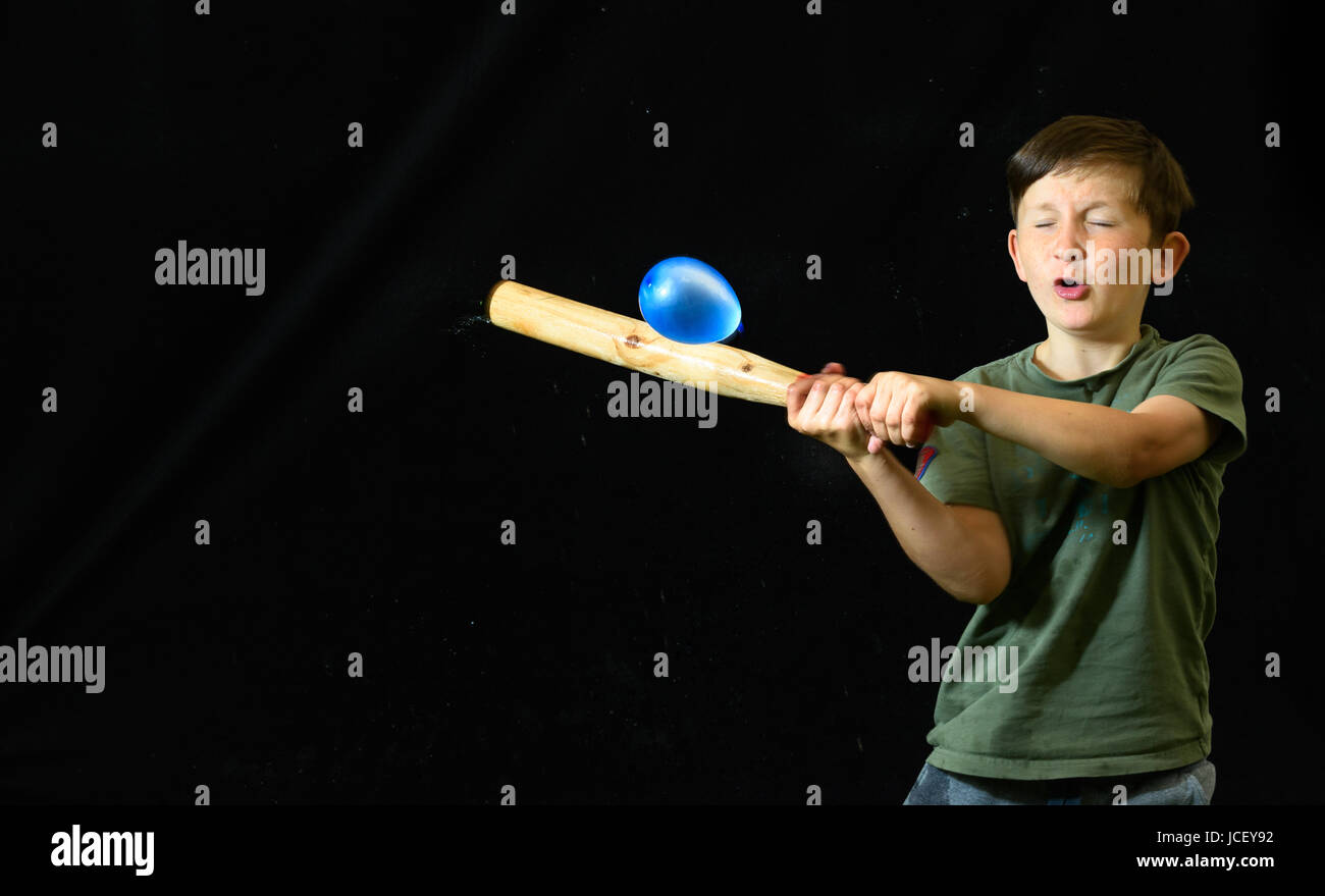 Ragazzo giovane a occhi chiusi e con un aspetto di incertezza sul suo volto, mira a rompere un palloncino di acqua con il suo bat. Foto Stock