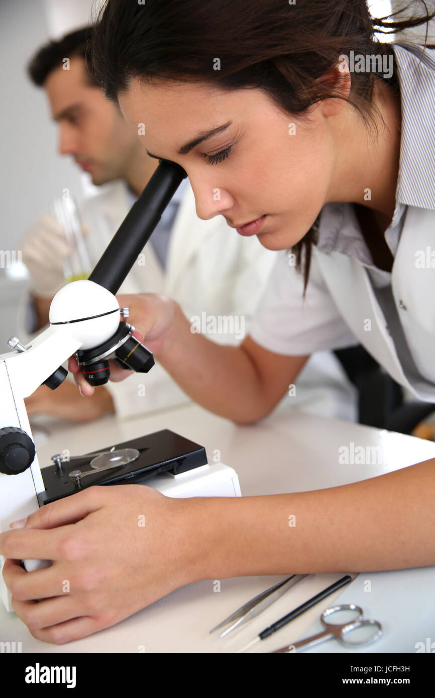 Giovane donna guardando attraverso la lente del microscopio Foto Stock