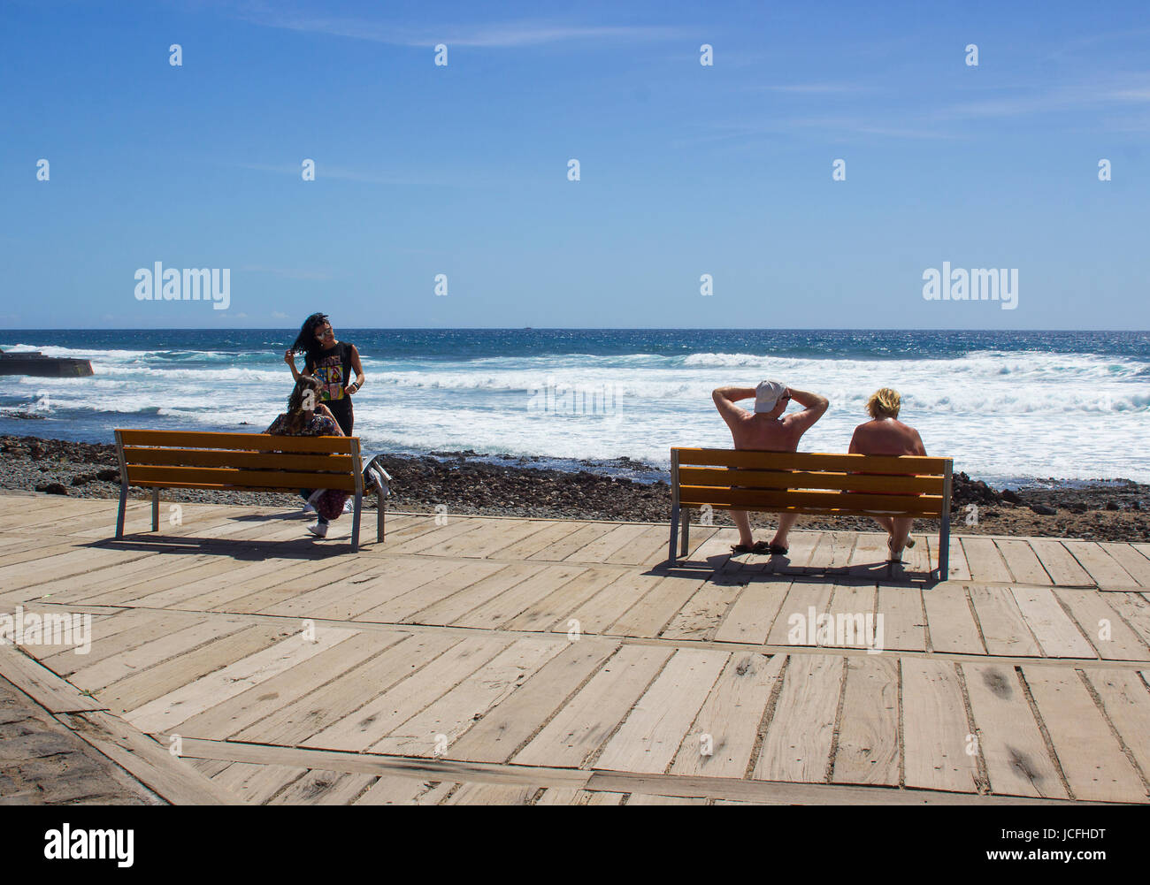 Le coppie relax su una terrazza in legno con vista sulla spiaggia in una calda giornata di sole in Playa Las Americas in Teneriffe spagnole nelle isole Canarie Foto Stock