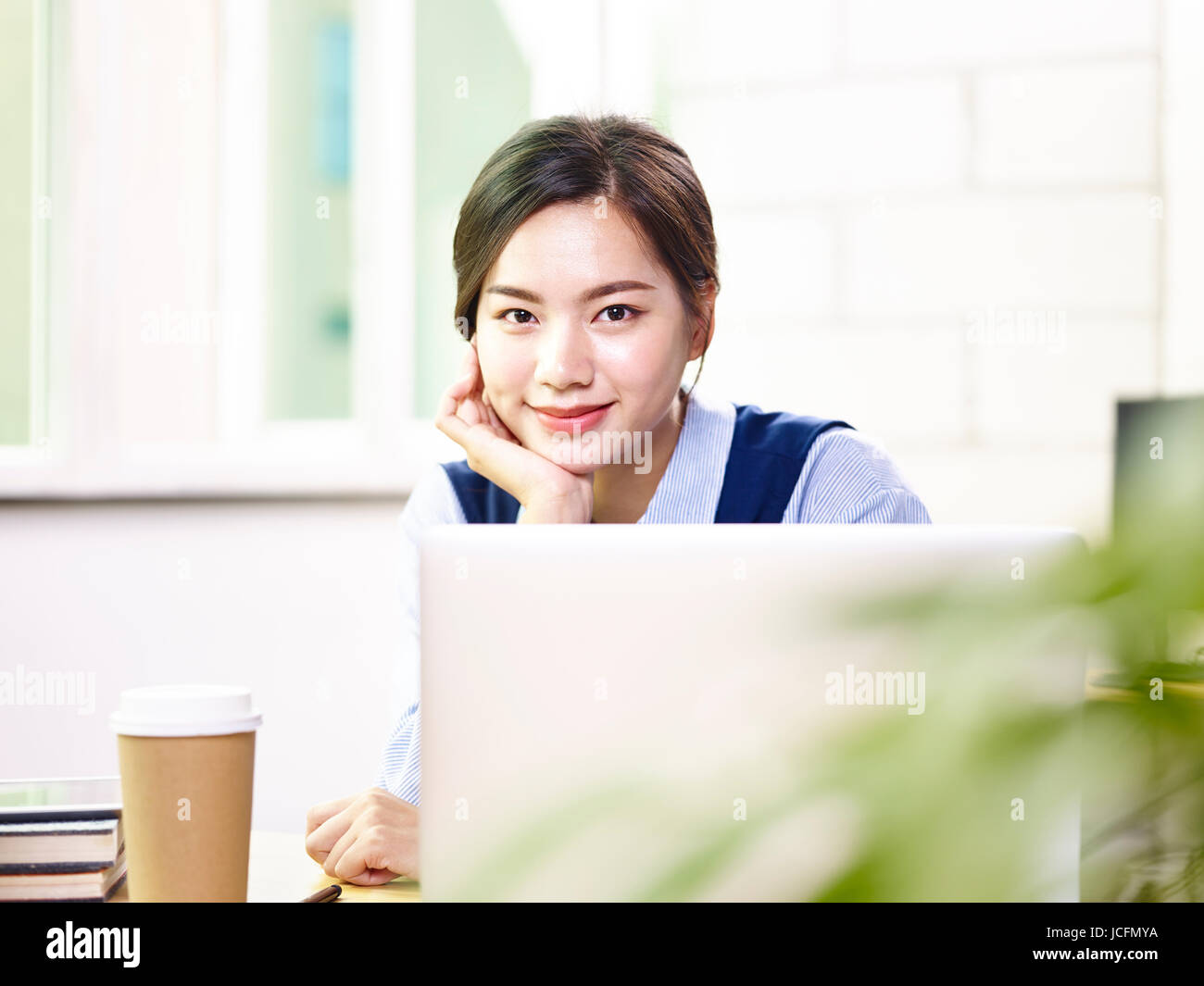 Giovani asian business donna seduta nella parte anteriore del computer portatile guardando la telecamera sorridendo. Foto Stock