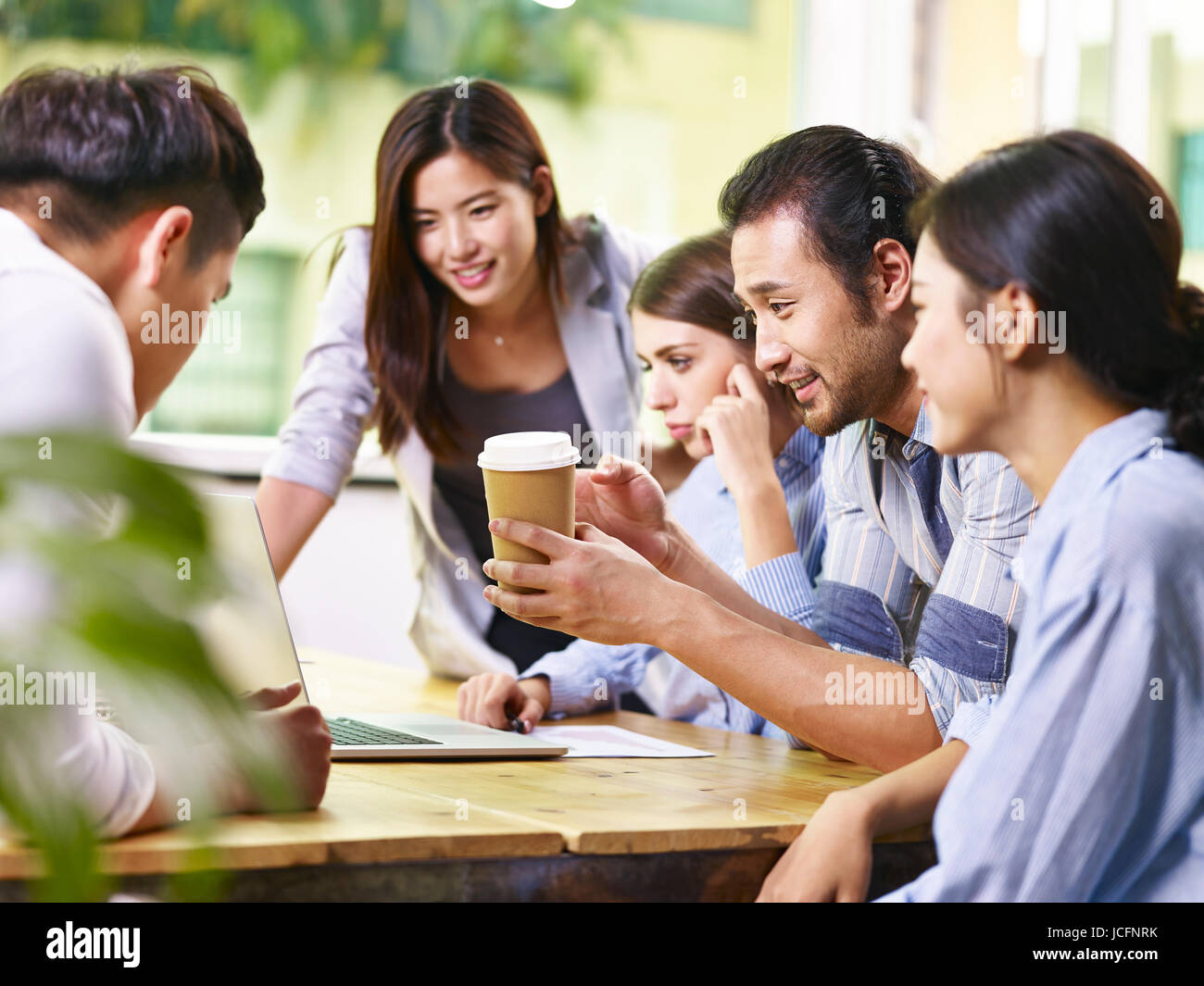 Un team di asiatici e caucasici imprenditori discutere di affari in ufficio utilizzando il computer portatile. Foto Stock