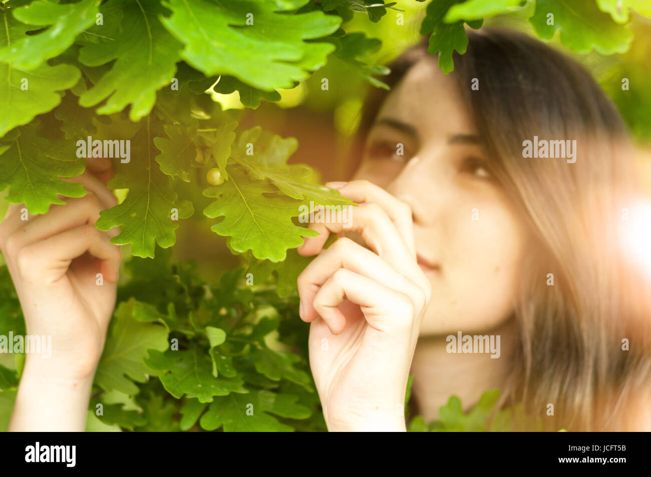 Bohemian girl godere in piedi la natura giocando con foglie di albero in presenza di luce solare Foto Stock