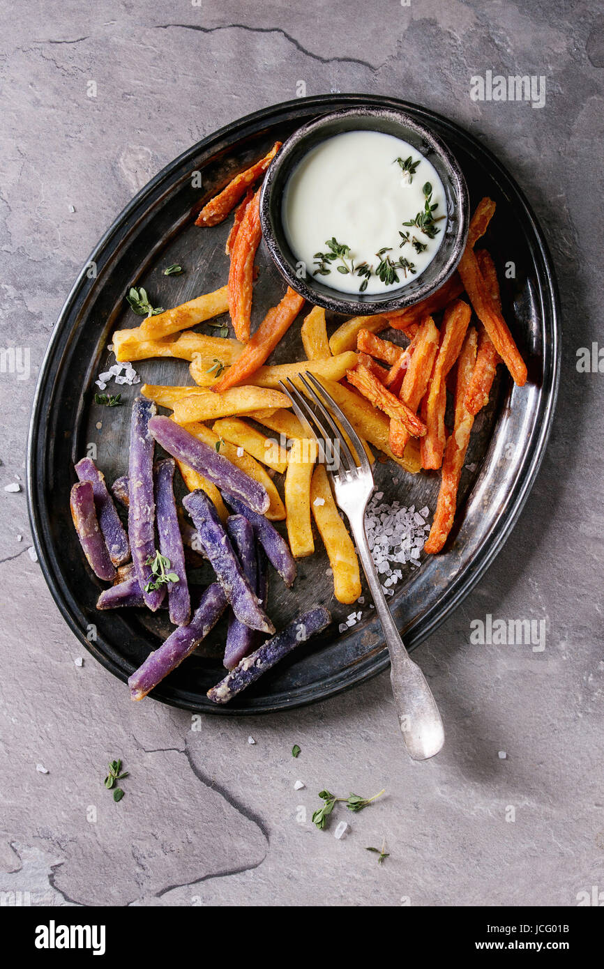 Varietà di patate fritte patate tradizionali, viola di patata, carota servito con il formaggio bianco salsa, sale, il timo sul vassoio vintage su texture grigio indietro Foto Stock