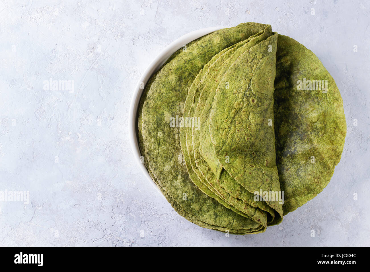 Pila di vuoto di spinaci Verde matcha tortillas nel piatto di terracotta su grigio Sfondo texture. Lay piatto con spazio di copia Foto Stock