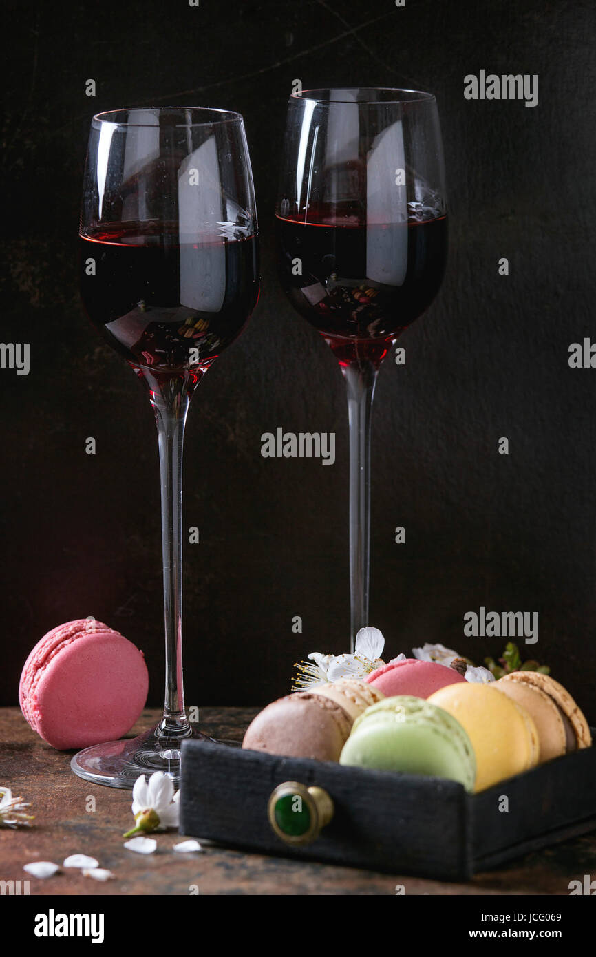 Due bicchieri di vino di Porto con una varietà di coloratissimi francese dessert dolci macaron amaretti con vari ripieni serviti con fiori di primavera oltre il buio Foto Stock