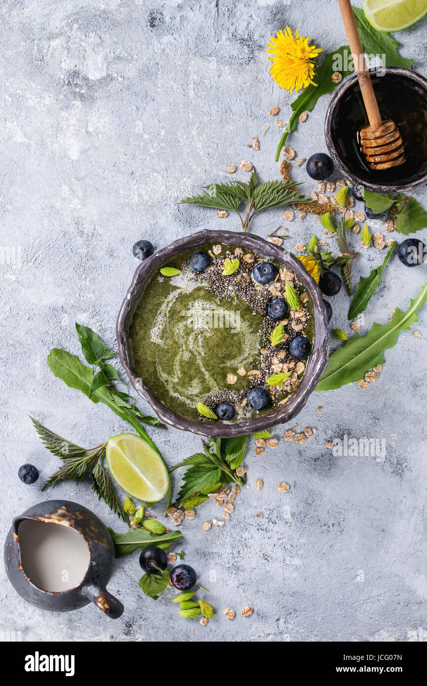 Verde primavera ortica e tarassaco ciotola smoothie servita con calce, fiori gialli, foglie giovani, fiocchi di avena, semi di Chia, mirtilli, la crema di latte e miele o Foto Stock