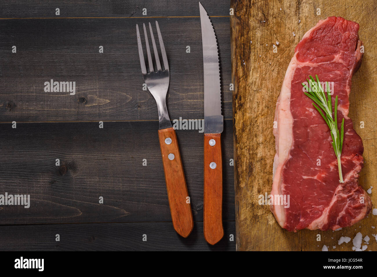 Materie di manzo bistecca di controfiletto al rosmarino forchetta e coltello sullo sfondo di legno vista superiore Foto Stock