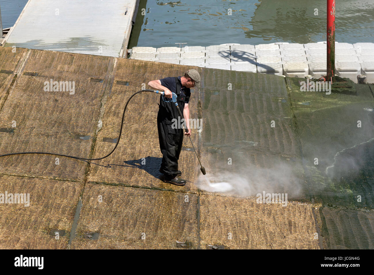 Uomo che utilizza un getto d'acqua per pulire le alghe verdi da un calcestruzzo marina uno scalo. Dorset Regno Unito Inghilterra Giugno 2017 Foto Stock