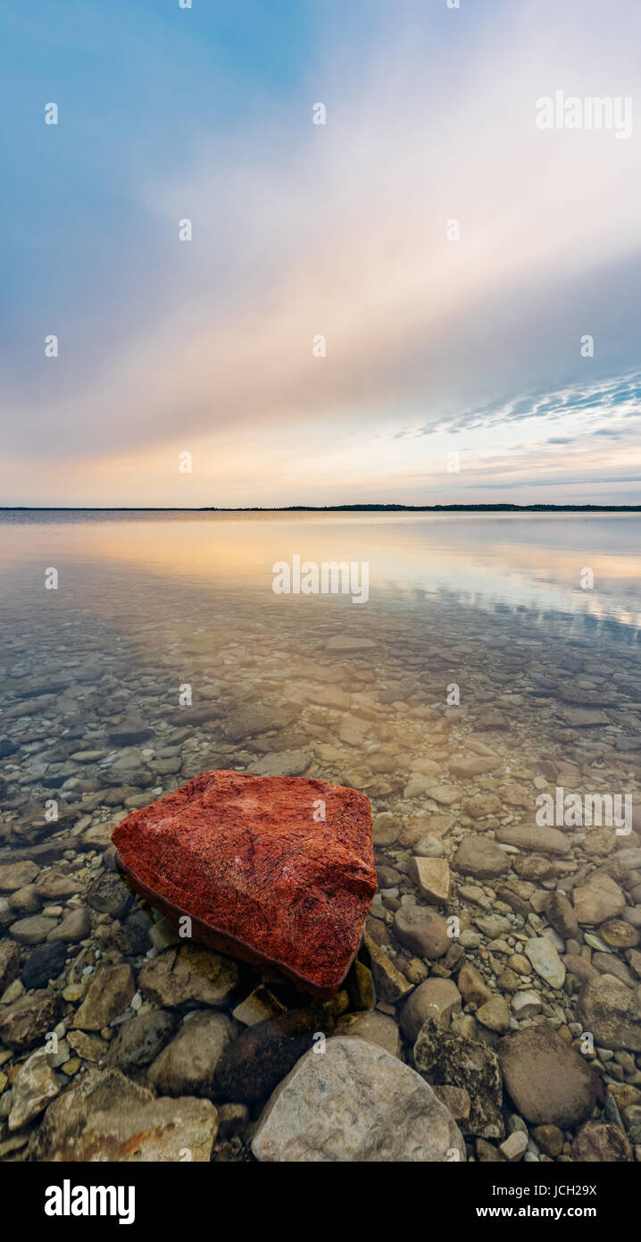 Mare calmo con acqua trasparente dalla splendida alba, vivid pietra rossa in primo piano. Lunga esposizione panorama verticale Foto Stock