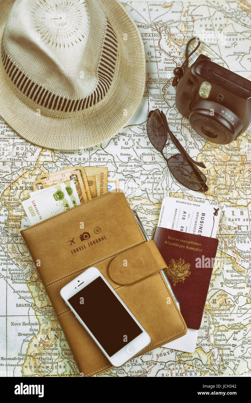 Un piatto di oggetti essenziali per il viaggio su una mappa antica, fotocamera istantanea, telefono cellulare con schermo nero, occhiali da sole, valute, passaporto, carta d'imbarco... Foto Stock